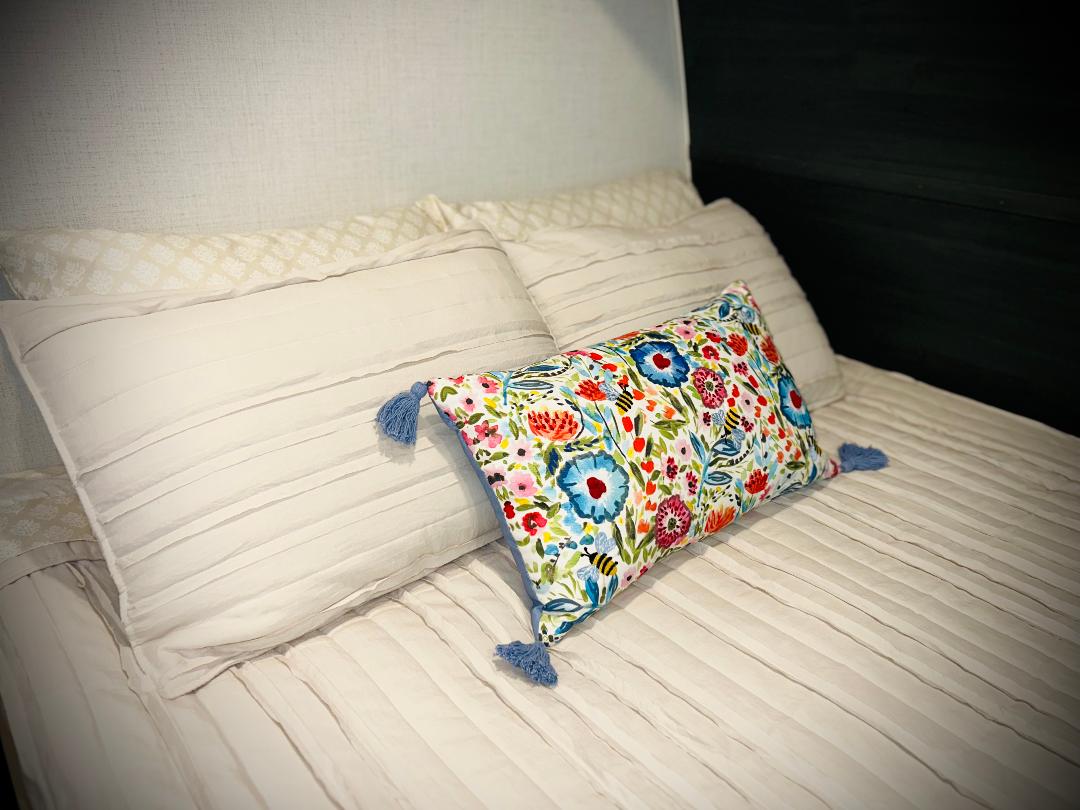 Cozy RV rental bedroom with white pleated bedding and a vibrant floral lumbar pillow.. Keystone RV Springdale Mini 1800BH 2024