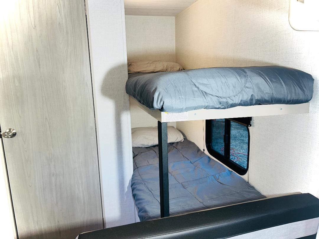 Cozy bunk beds inside an RV rental with grey bedding, a light wood door, and window. Ideal for a family camper.. Keystone RV Springdale Mini 1800BH 2024