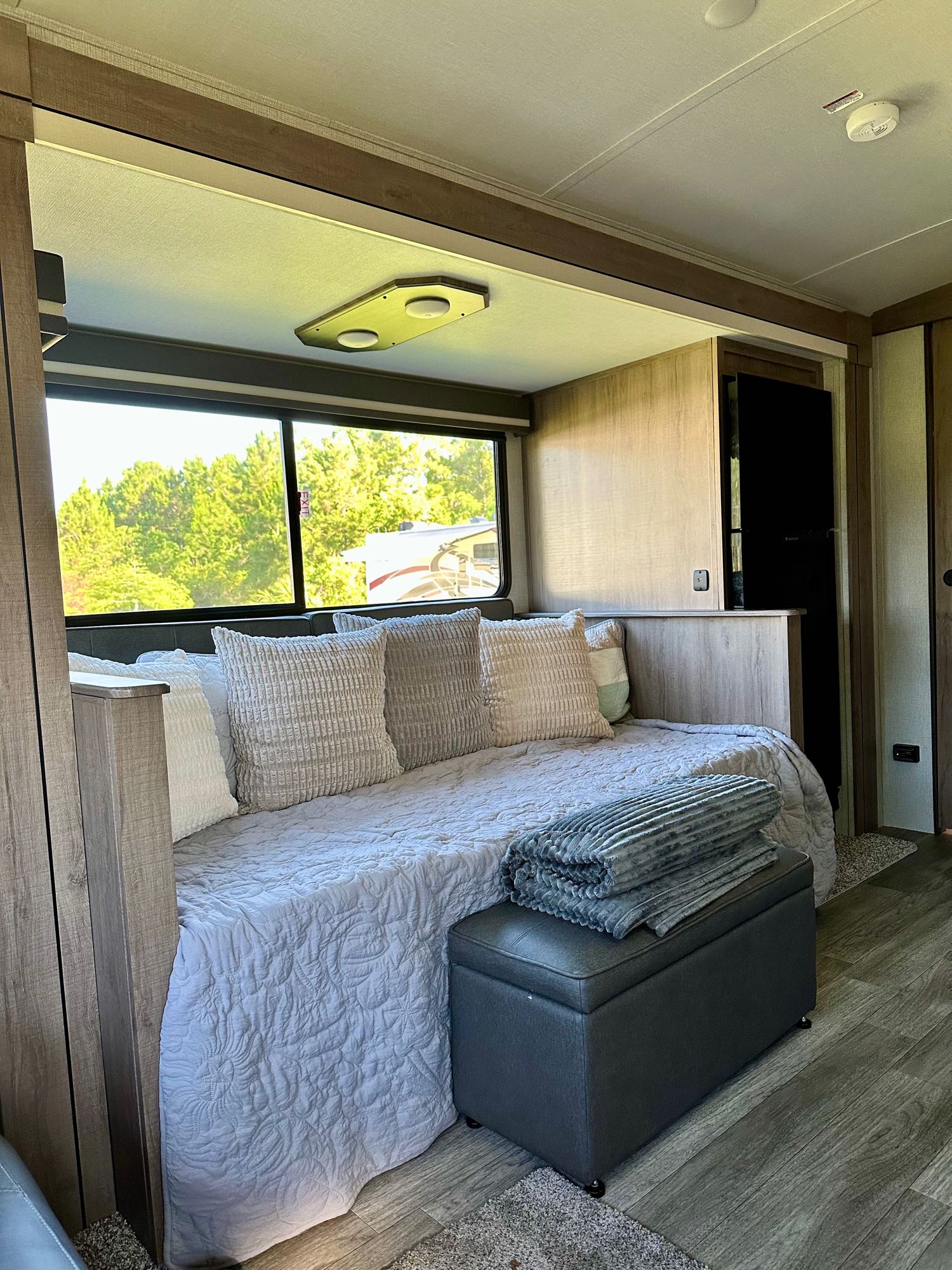Cozy RV rental interior: daybed with soft pillows, blanket, and scenic window view for travel comfort.. Grand Design Imagine 2023