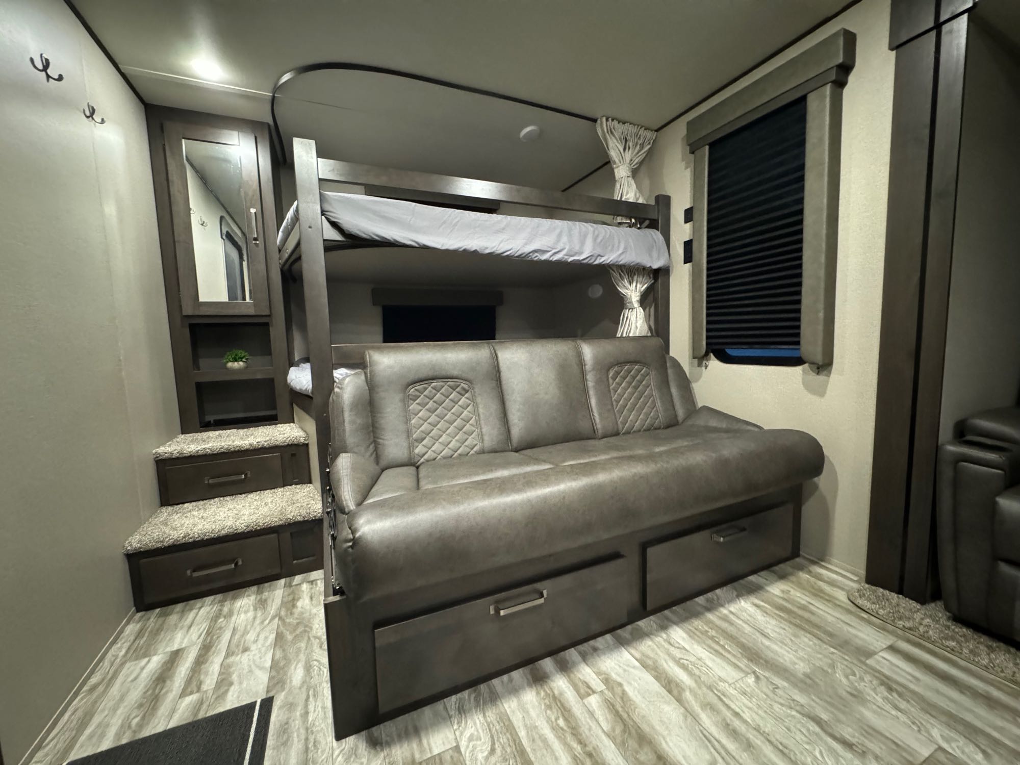 View inside an RV rental, featuring bunk beds, a sofa with under-storage, and carpeted steps.. Grand Design Transcend Xplor 2022