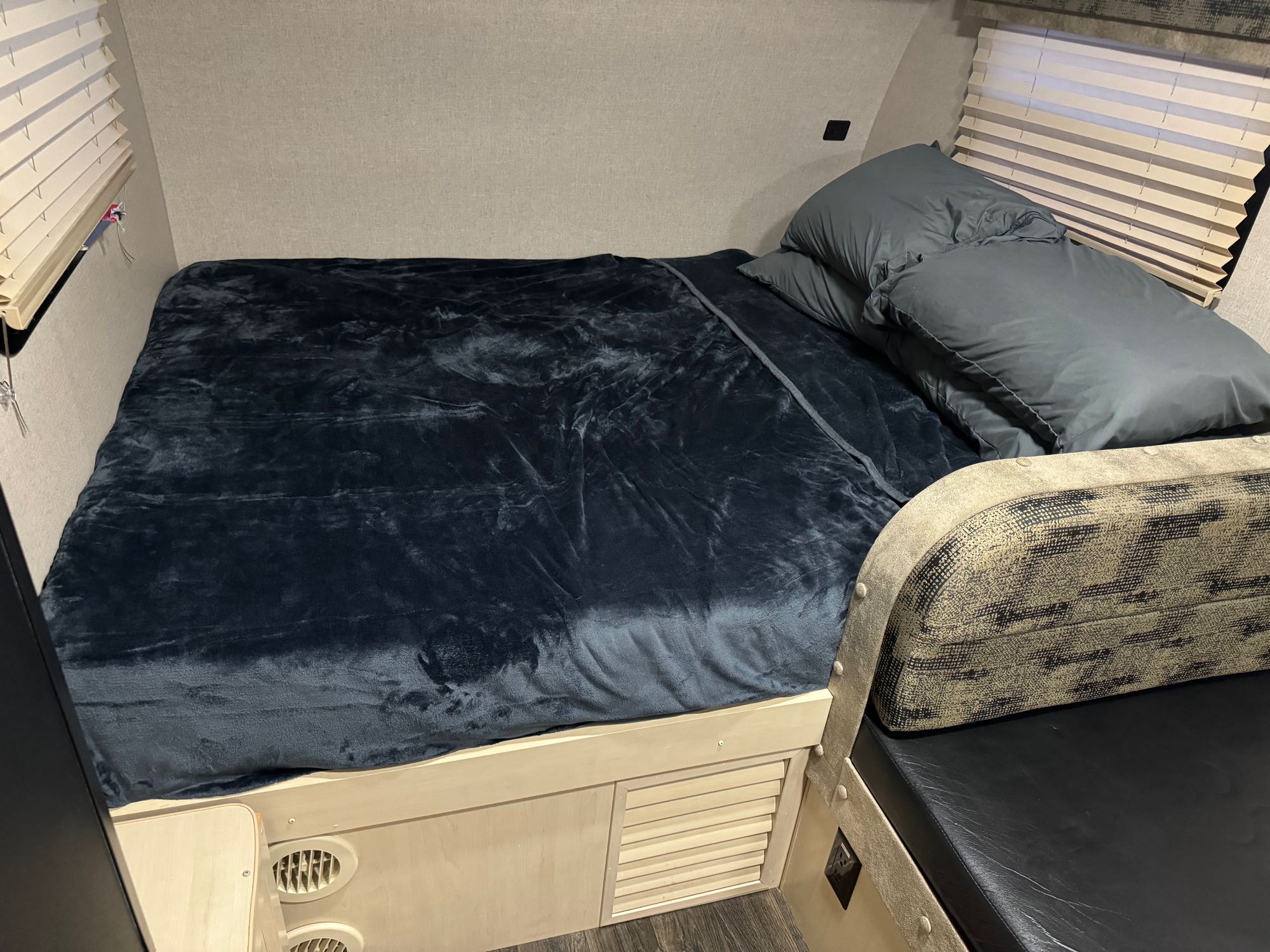 Comfortable RV rental sleeping area with dark blue blanket, pillows, and an adjacent patterned bench seat and window blinds.. Minnie Minnie Drop 2019