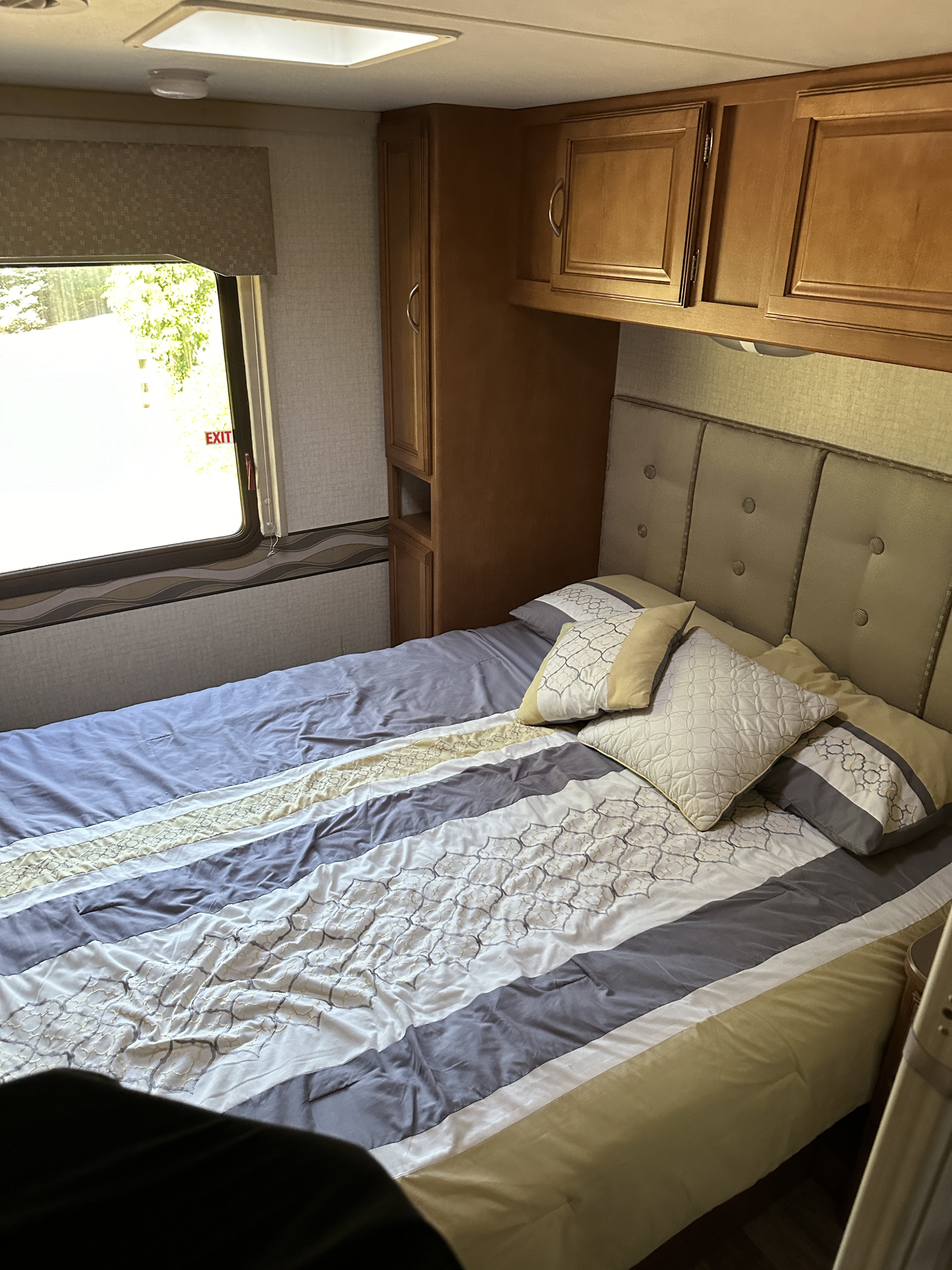 Experience comfort in this RV rental bedroom. Features a cozy bed with patterned linens, overhead cabinets, and an exit window.. Winnebago Minnie Winnie 2017