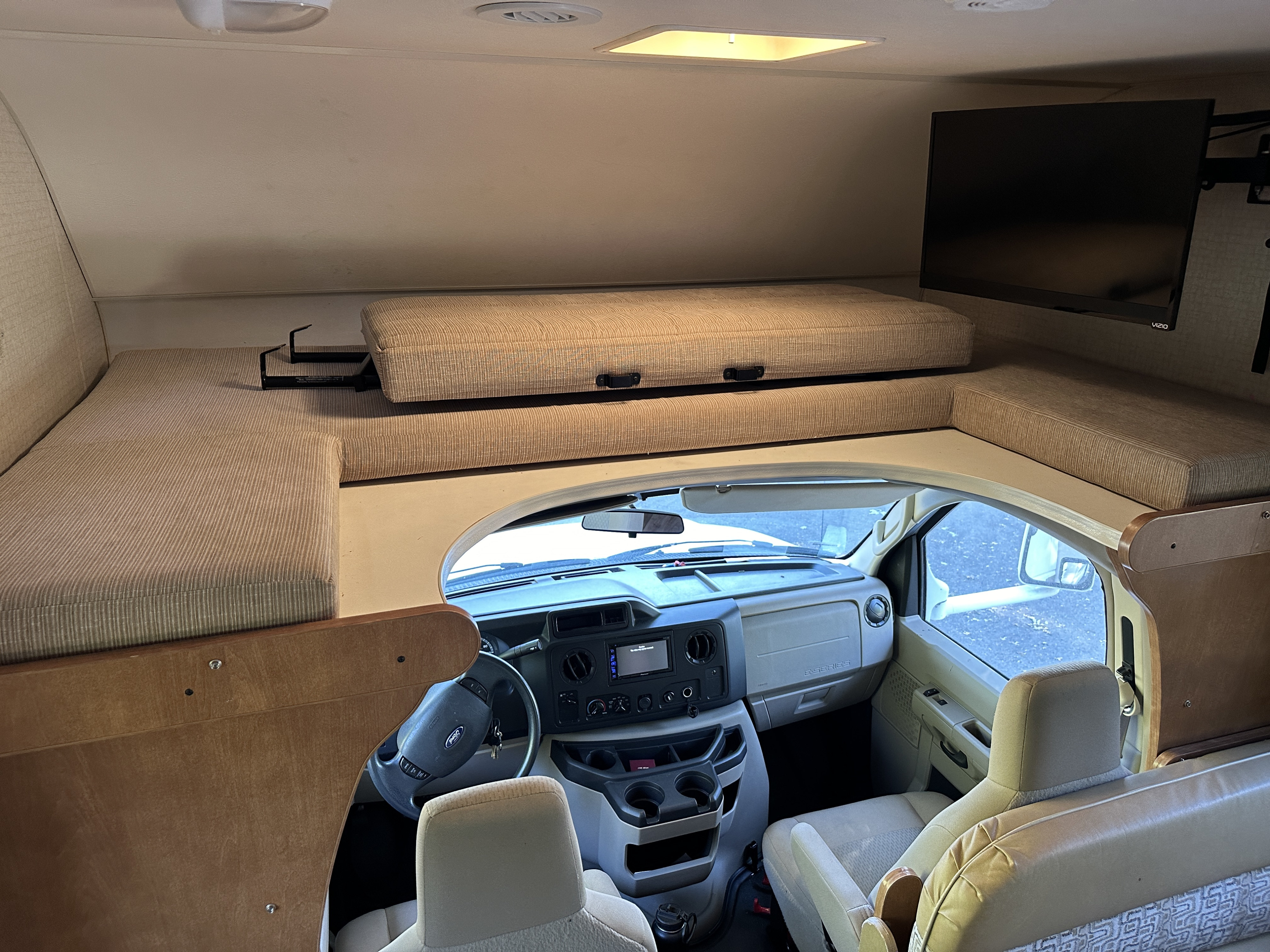 Spacious RV rental interior featuring an overhead bunk bed, comfortable cockpit, and mounted TV. Ideal for road trips.. Winnebago Minnie Winnie 2017