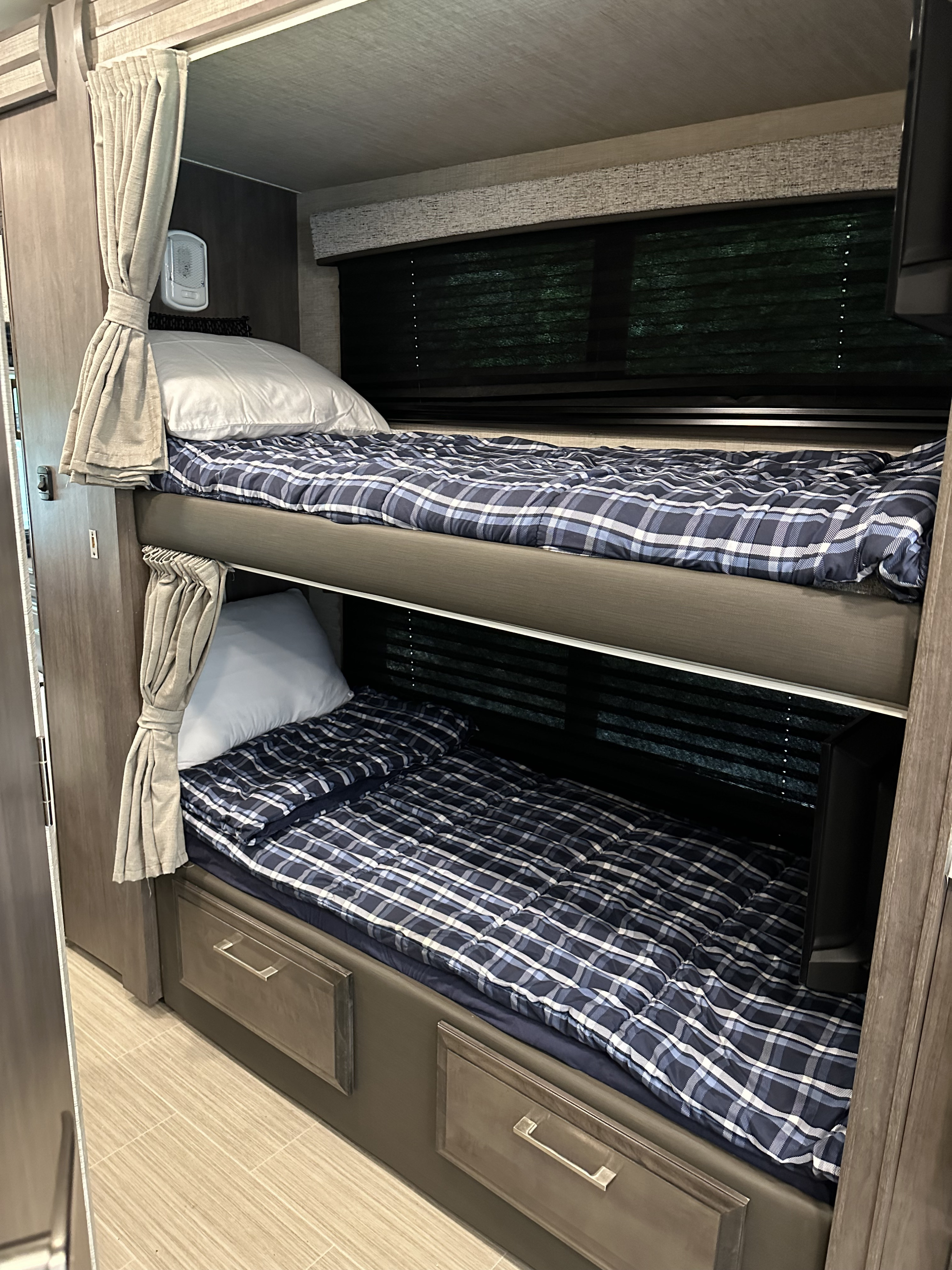 Comfortable RV rental bunk beds with blue plaid comforters, white pillows, window blinds, and built-in storage.. Entegra Coach Odyssey 2022