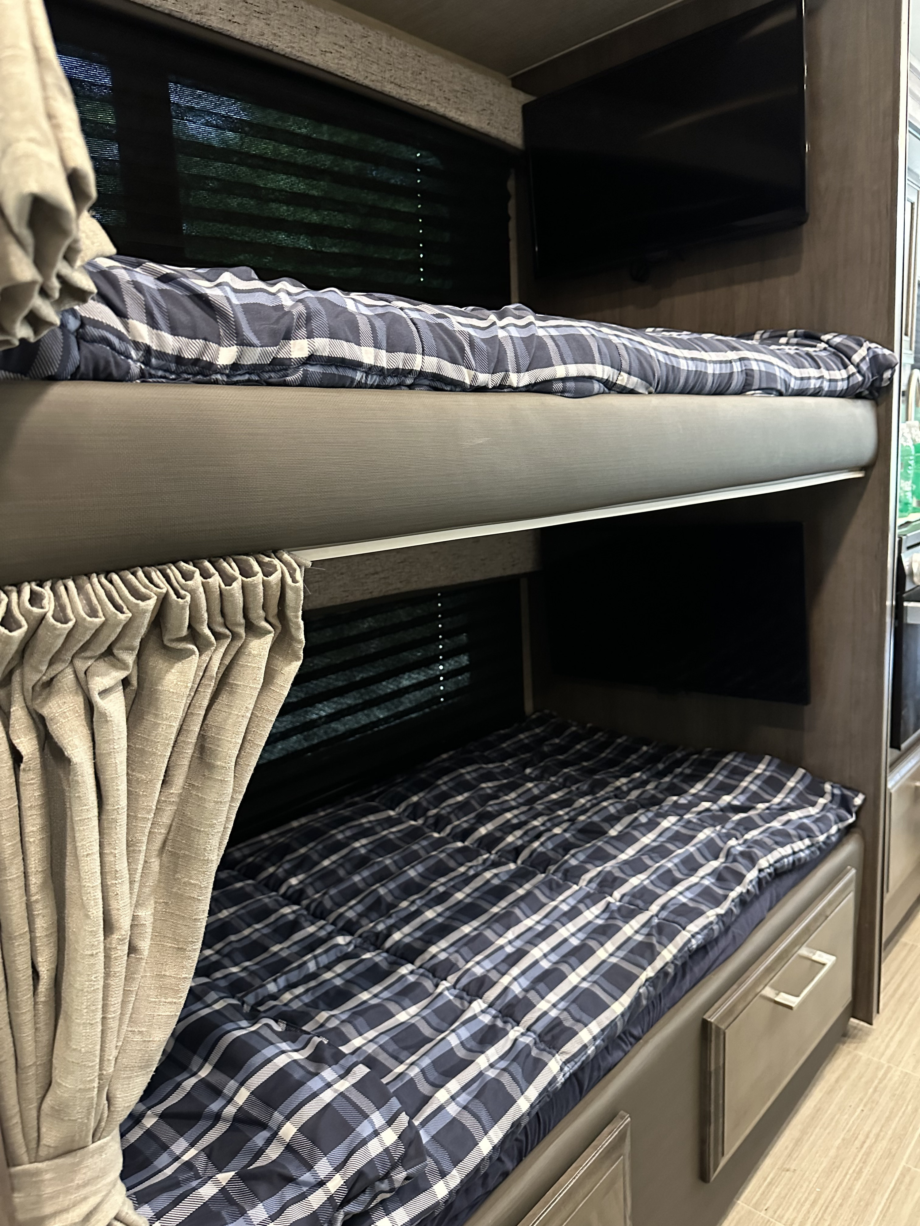 Cozy RV rental bunk beds with plaid bedding, privacy curtains, and TVs, ideal for travel accommodation.. Entegra Coach Odyssey 2022