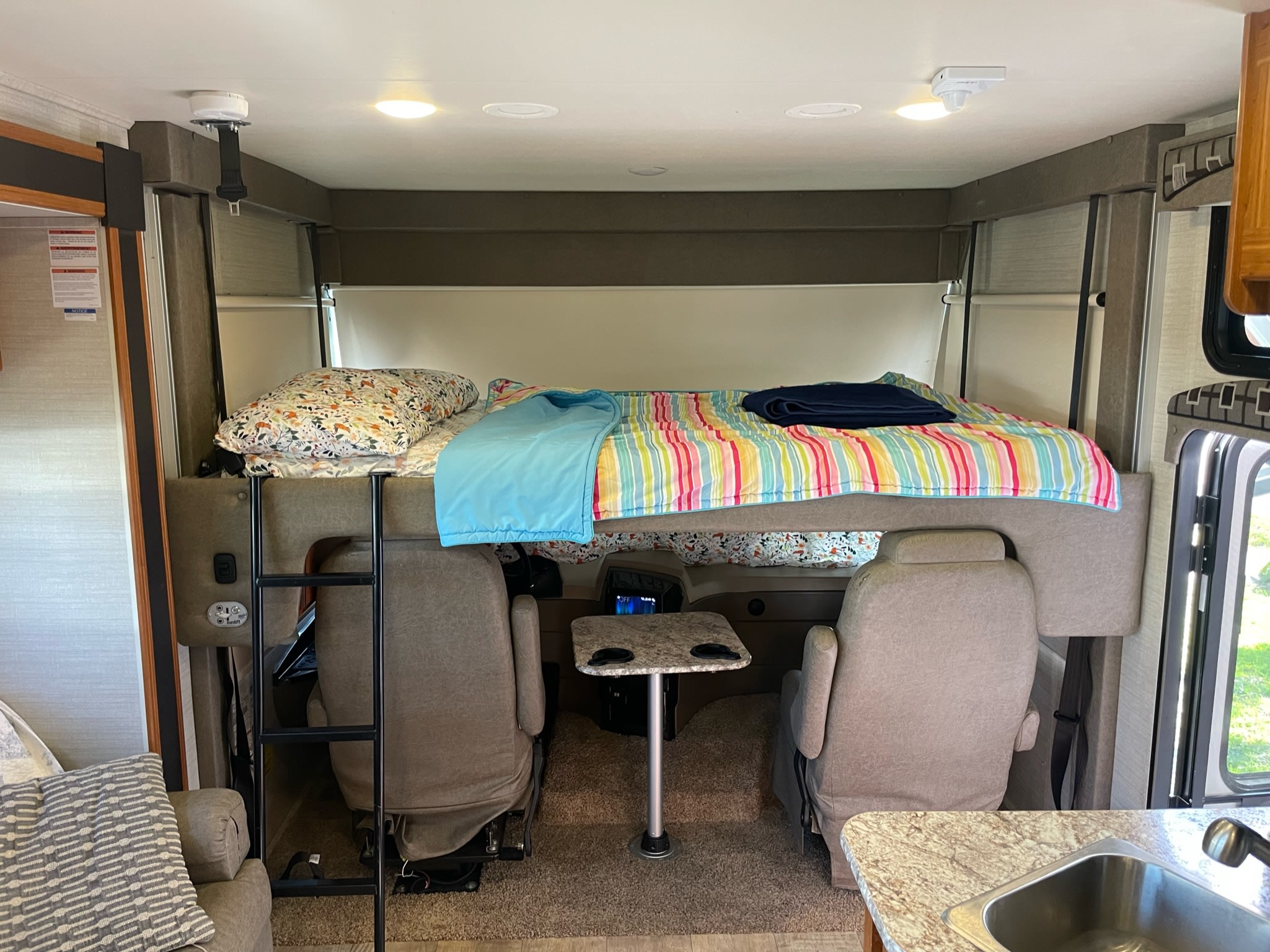 Cozy RV rental interior with a cab-over bunk bed, colorful bedding, access ladder, and swiveling driver/passenger seats.. Jayco Alante 2017