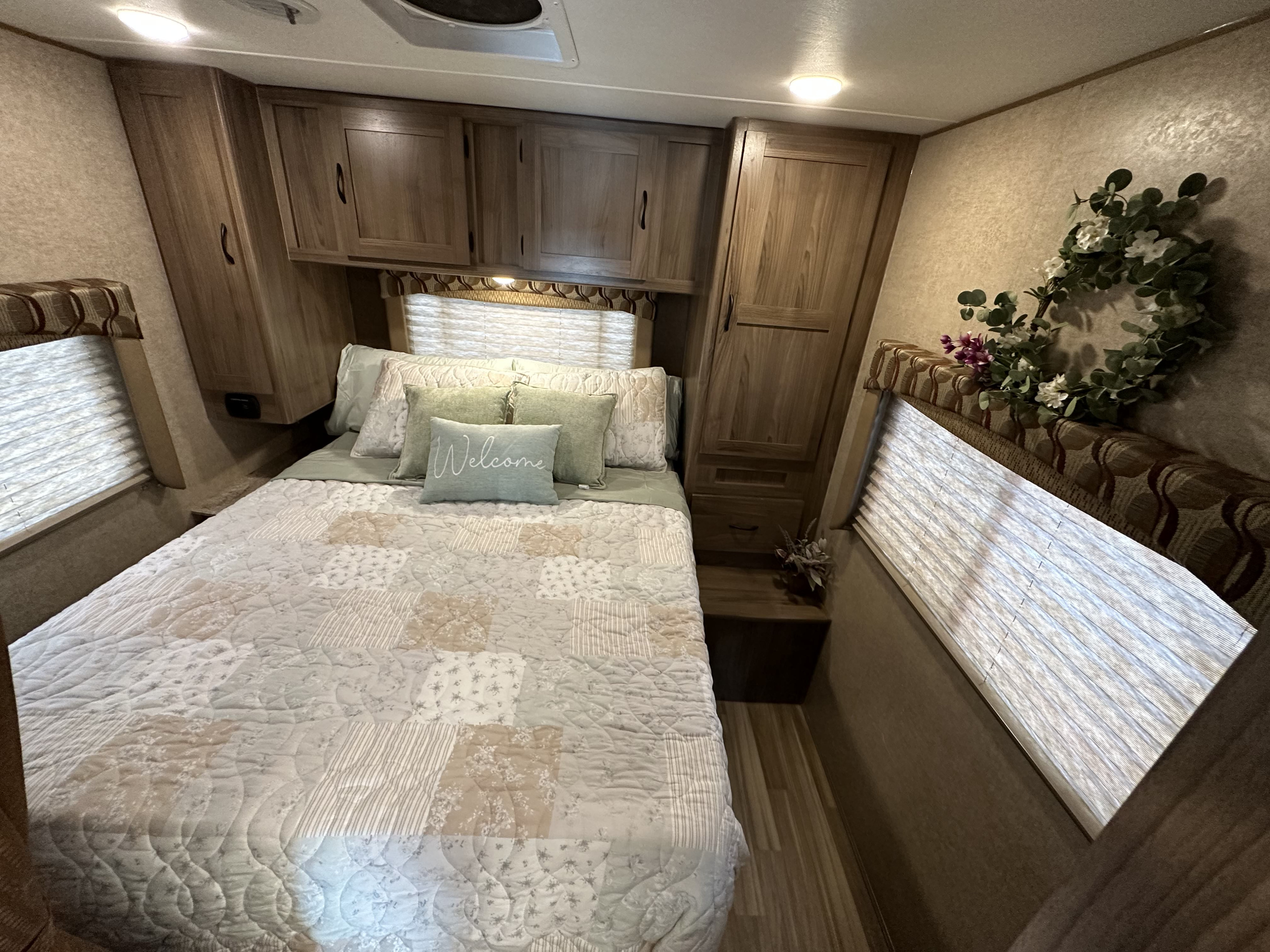 Cozy RV rental bedroom with a comfy bed, "Welcome" pillow, overhead cabinets, and soft lighting, ideal for travel.. Coachmen Freelander 2017