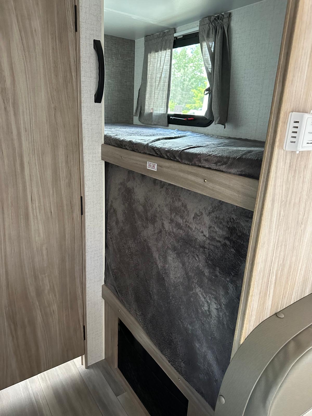 Cozy RV rental interior with bunk beds, showing the top bunk's 250 lbs limit and a window with curtains.. Winnebago Micro Minnie 2022
