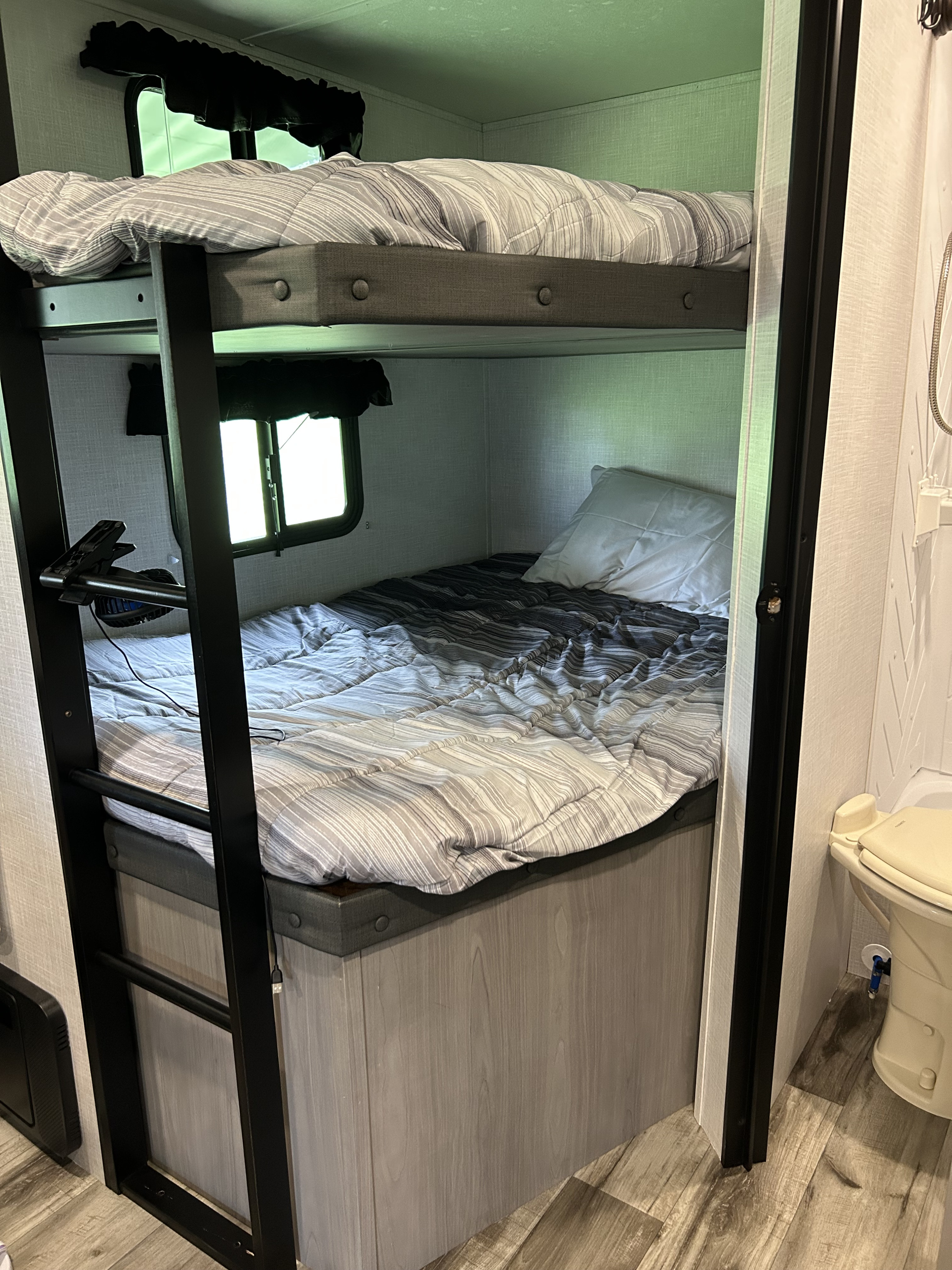RV rental interior featuring comfortable bunk beds with striped bedding, a window, and a compact adjacent bathroom.. Dutchmen Coleman Lantern LT 2022