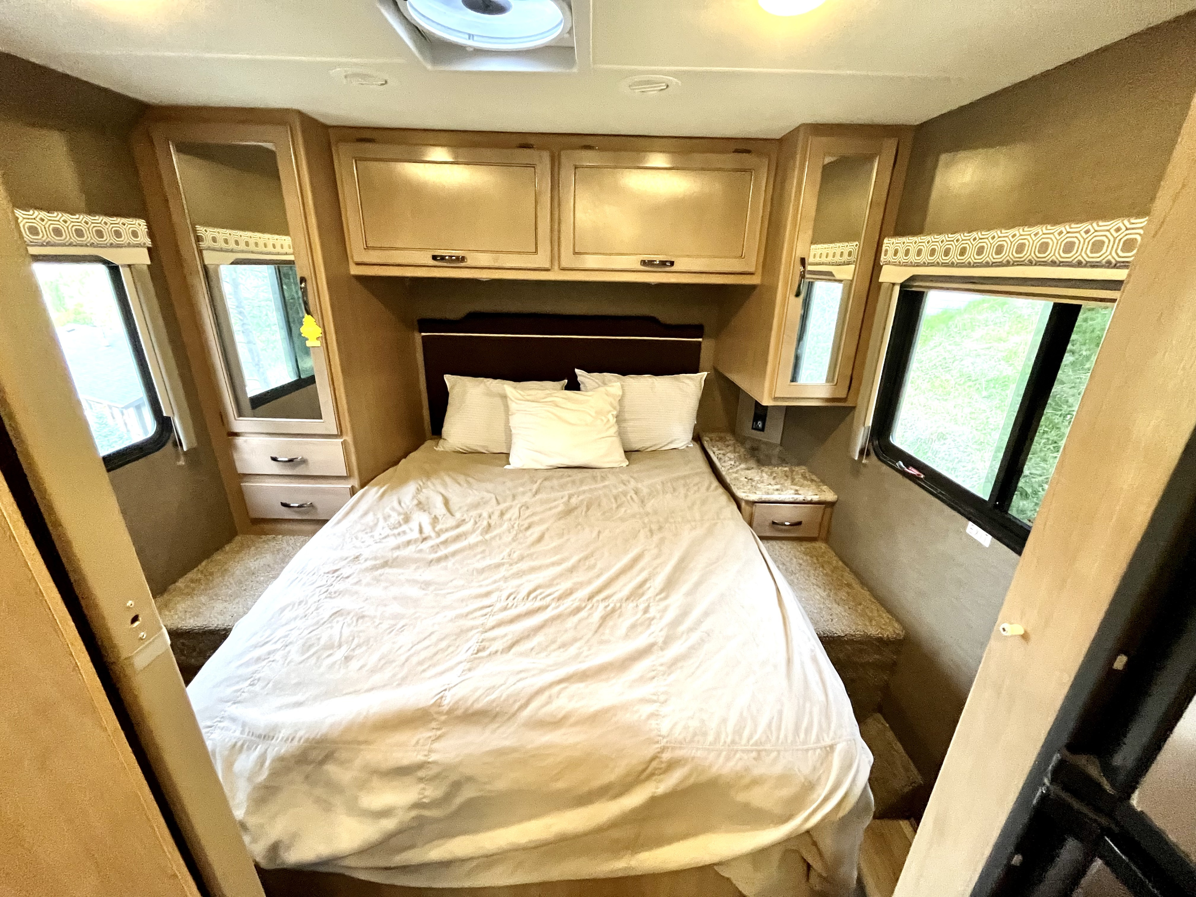 A comfortable RV rental bedroom interior with a neatly made bed, overhead storage, and side windows, perfect for your travels.. Thor Four Winds 2020