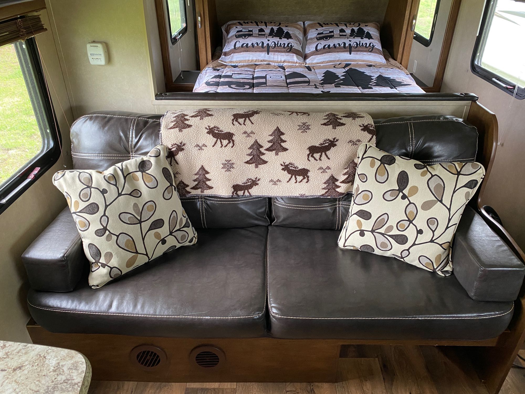 Relaxing RV rental interior: brown couch with nature-themed pillows & moose blanket, plus a "Happy Camping" bed.. Forest River Salem Cruise Lite 2017