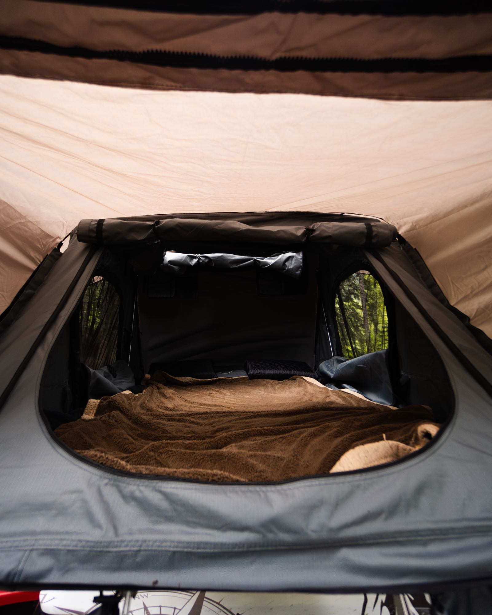 Inside a comfortable rooftop tent setup with a cozy blanket, offering forest views. Ideal for your next RV rental trip.. Chevrolet Open Road 2024
