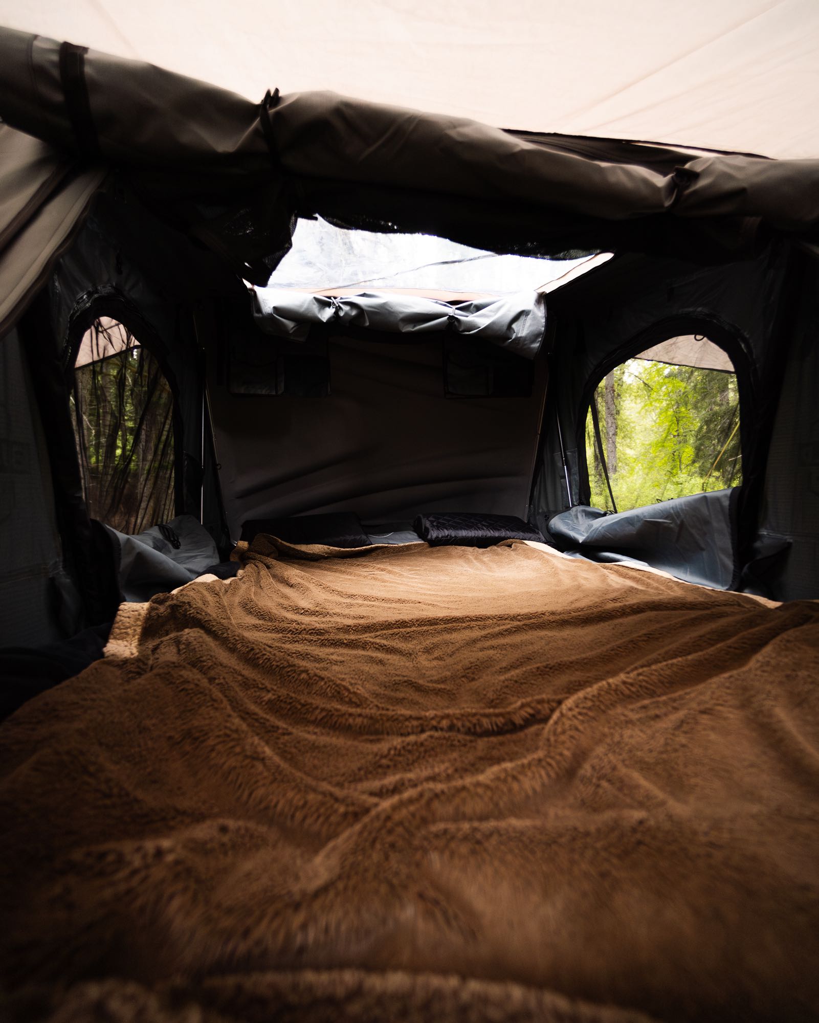 Cozy RV rental sleeping area with a plush brown blanket and forest views. Perfect for outdoor adventures and camping!. Chevrolet Open Road 2024