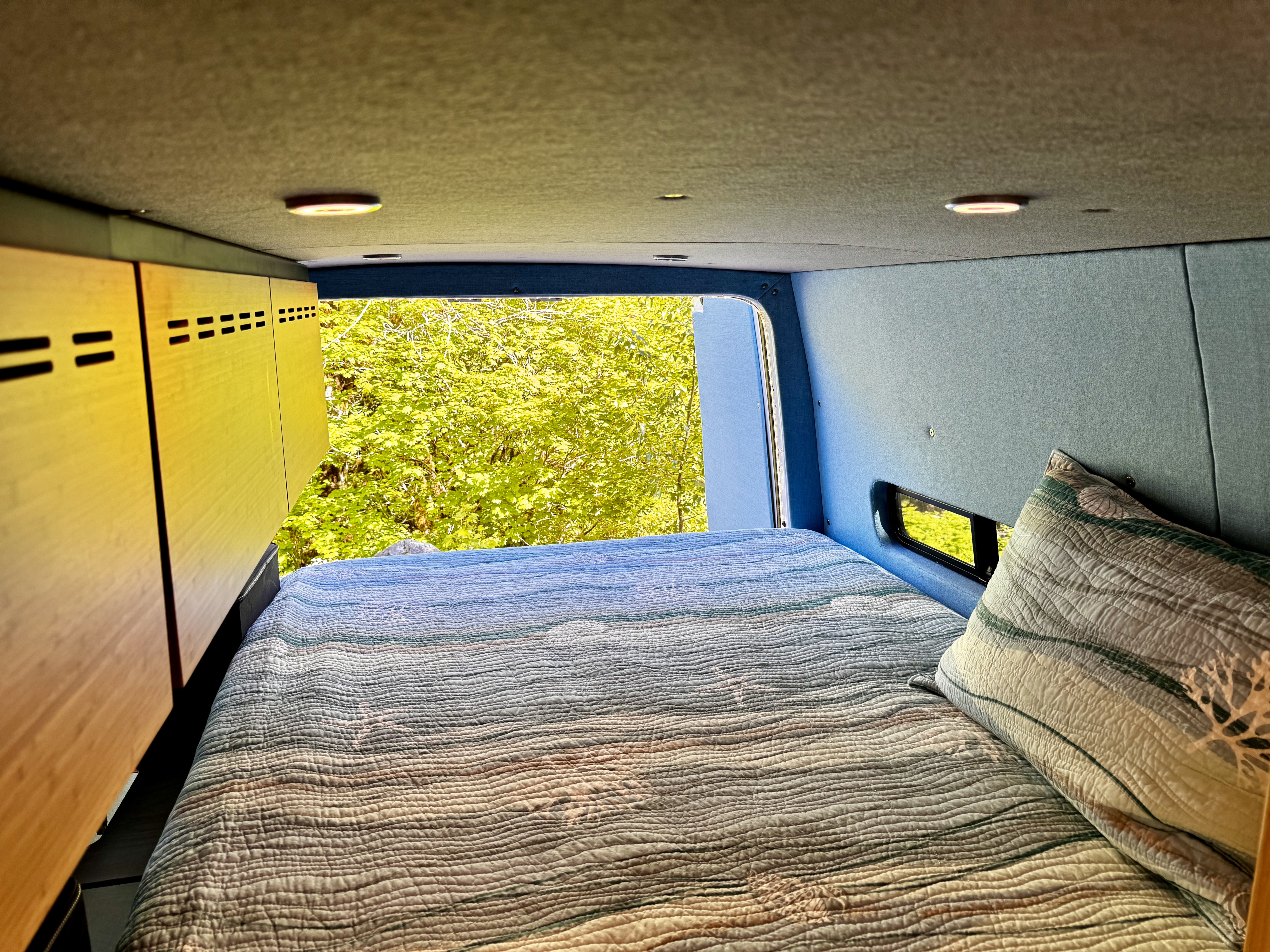 Inside this cozy RV rental, a comfy quilted bed faces lush green nature views through the open back.. Mercedes Sprinter 2017