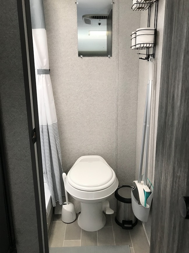 RV rental bathroom with a toilet, shower curtain to the left, mirror above, and wall storage on the right.. Forest River Salem FSX 2021