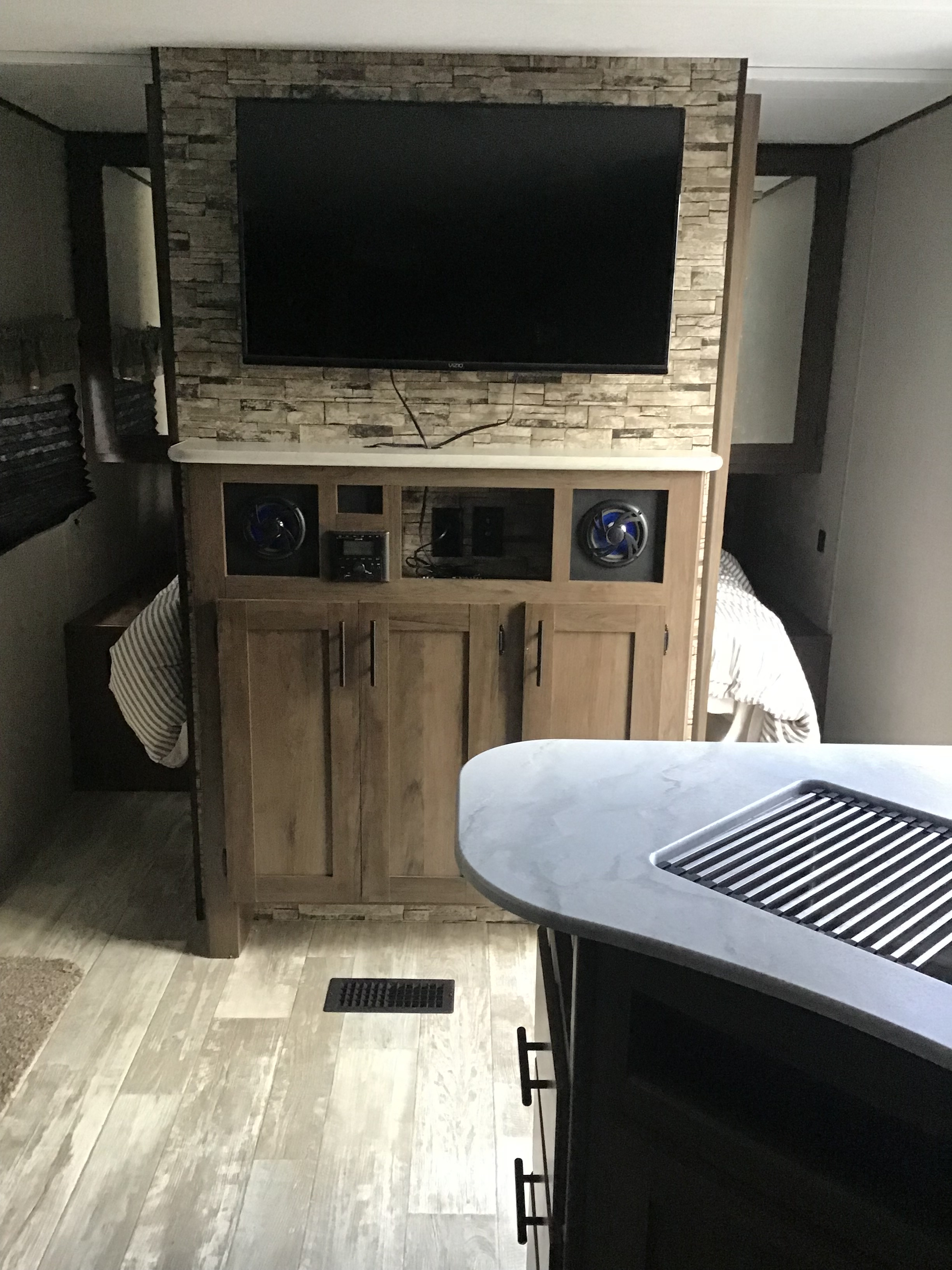 An rv rental living space with a TV on a stone accent wall, built-in entertainment system, and bedroom access.. Prime Time Avenger 2021