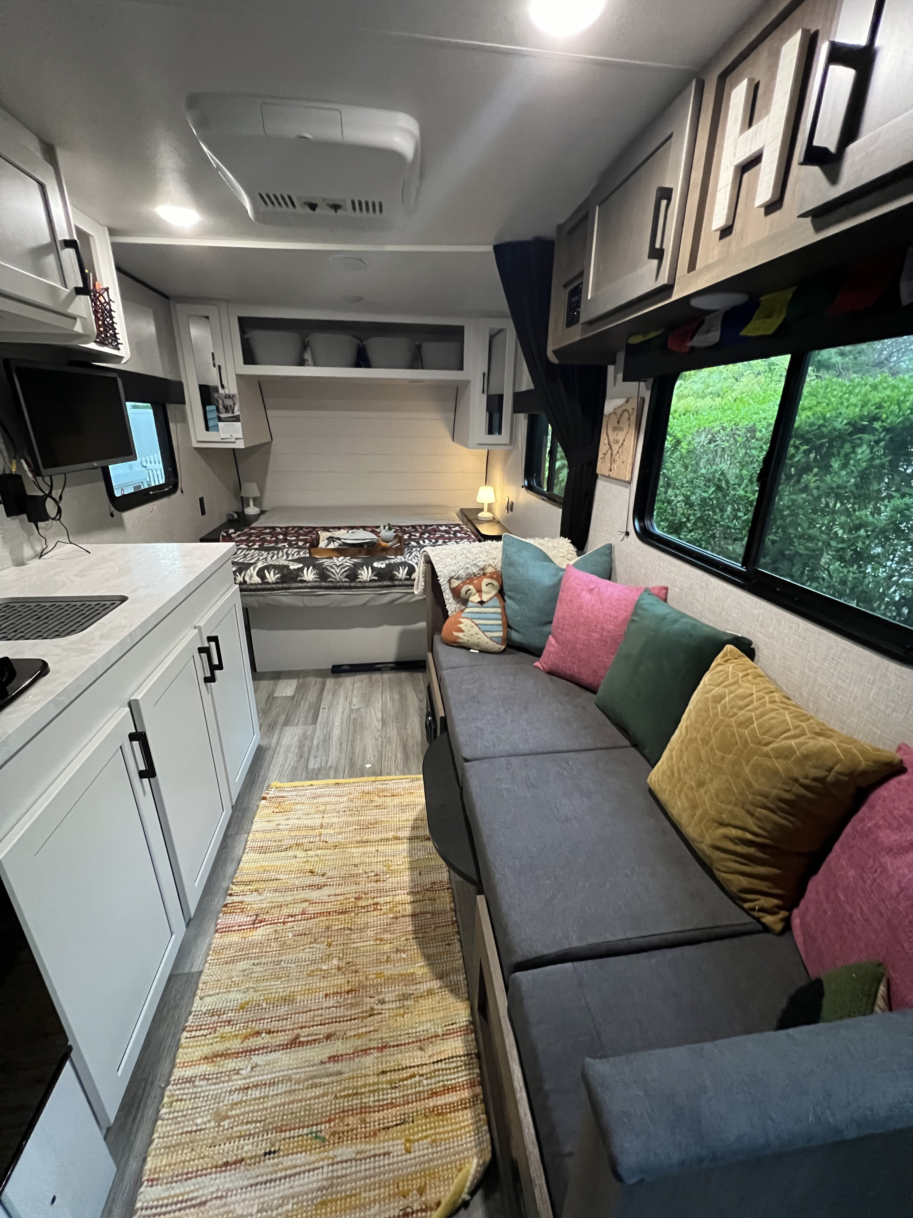 Vibrant RV rental interior featuring a gray couch with colorful pillows, bed, and kitchenette, offering a cozy retreat.. Jayco Jay Flight SLX 2024