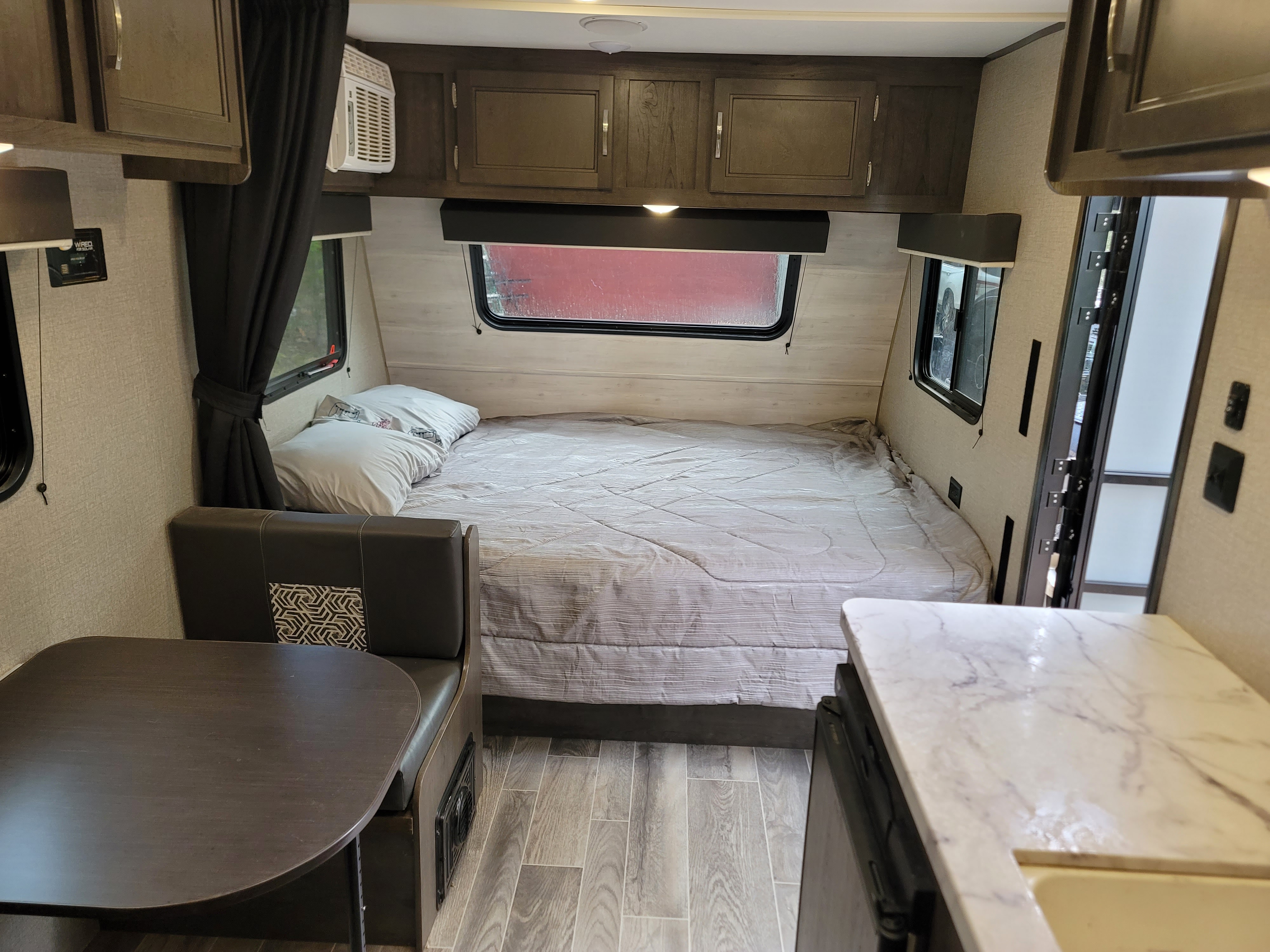 This RV rental interior shows a full bed, dining table, and partial kitchen counter, offering compact comfort.. Jayco Jay Flight SLX Baja Edition 2021