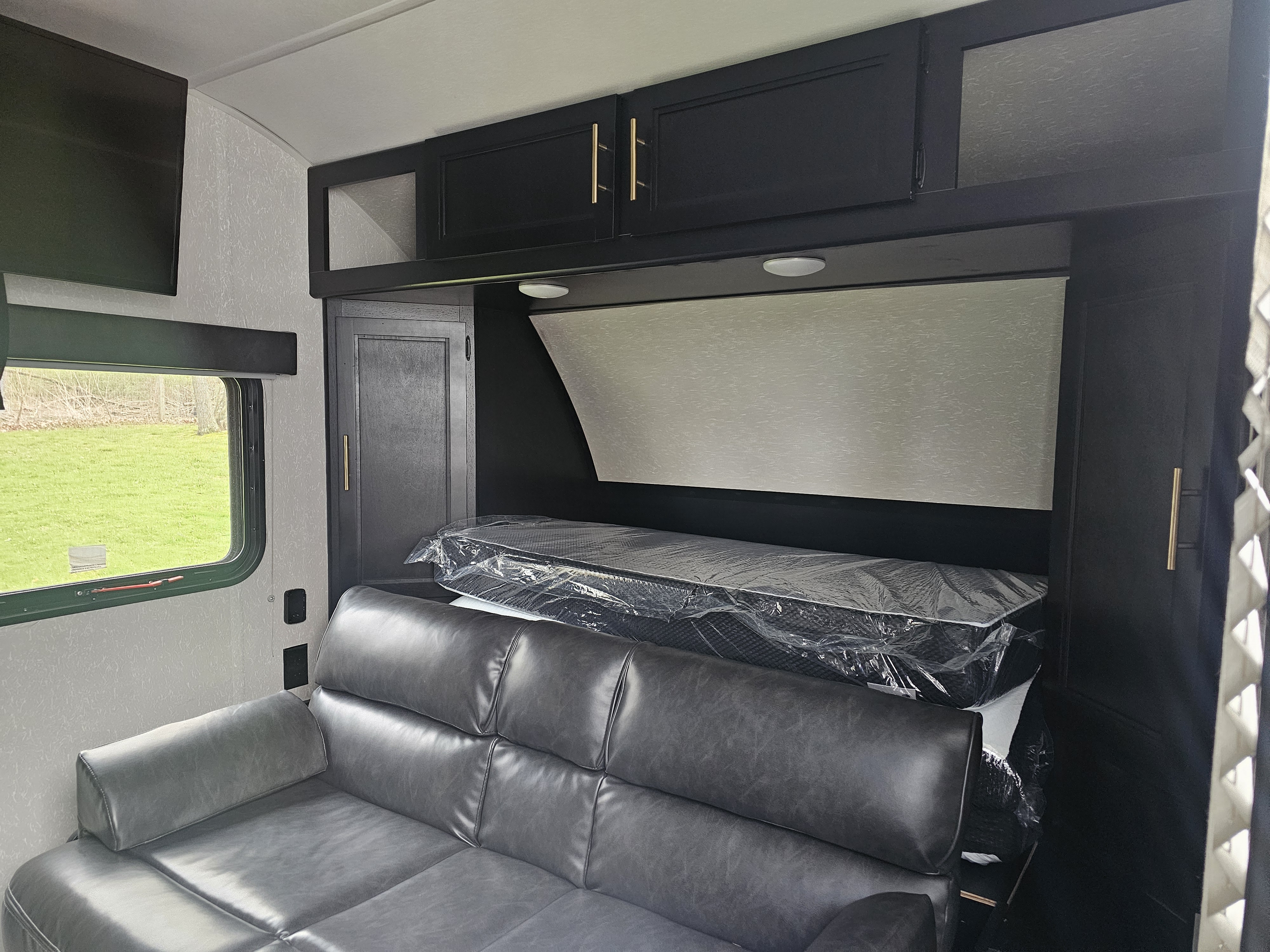 Explore this RV rental's modern interior: comfy sofa, new bed (still wrapped), black overhead cabinets, and a scenic window.. Forest River Cherokee Wolf Pup Black Label 2021