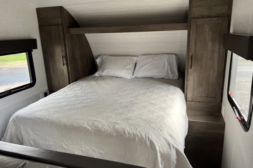 Inside an RV rental: a cozy bedroom with a neatly made queen bed, white pillows, and built-in storage on each side.. Forest River 268bh 2022