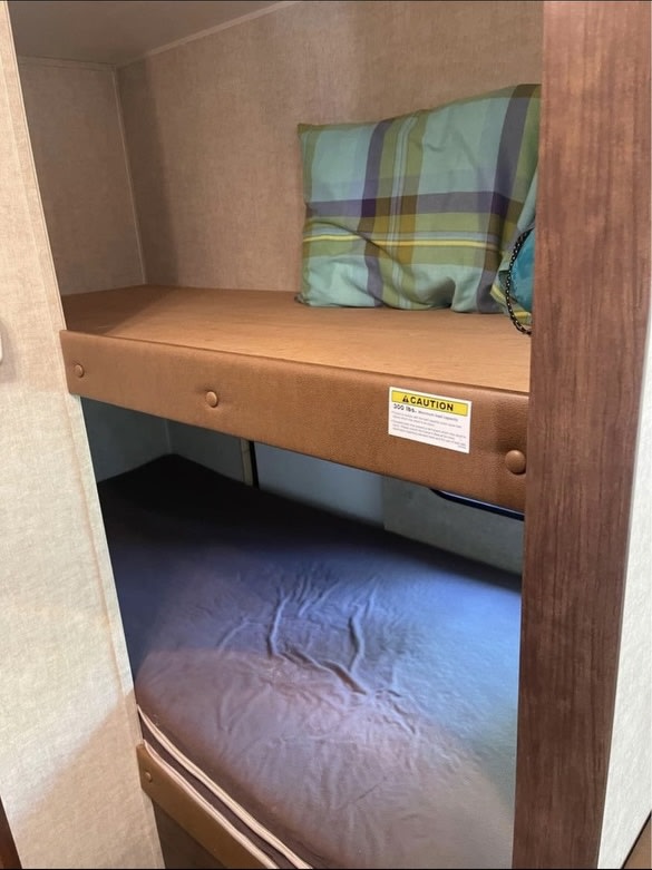 RV rental with cozy bunk beds. Upper bunk features a mattress, pillow, and "CAUTION 200 LBS" sticker. Lower bunk below.. Keystone RV Hideout 2016