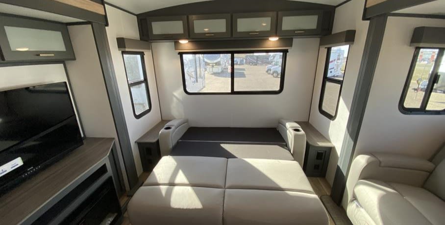 This RV rental interior features a convertible sofa bed, large windows, overhead cabinets, and a TV with fireplace.. Keystone RV Bullet Premier Ultra Lite 2022