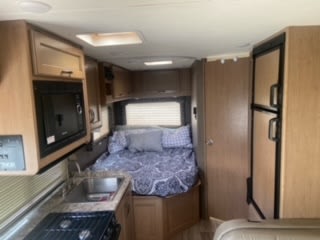 RV rental interior featuring a compact kitchen, bedroom with patterned bedding, and refrigerator, ideal for travel.. Thor Four Winds 2020