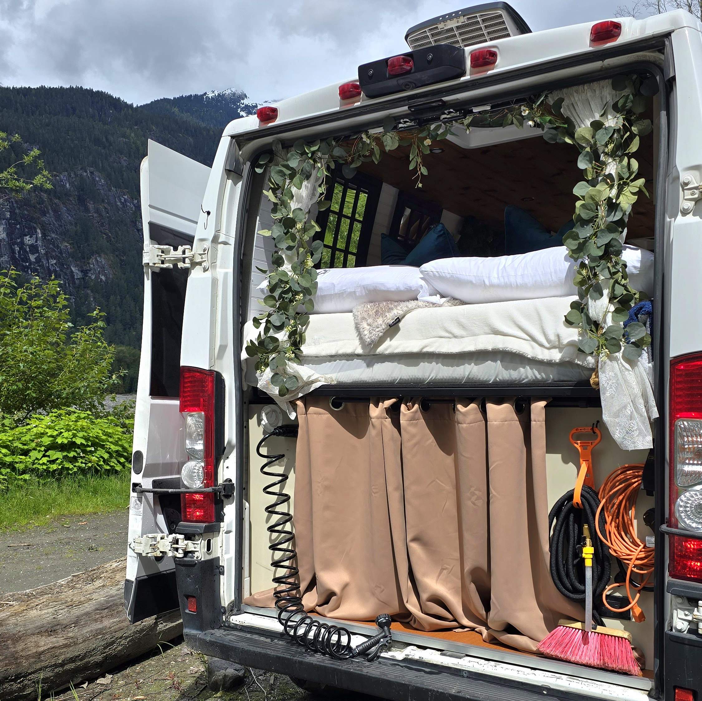 Cozy **rv rental** camper van with open back doors showcasing a comfortable bed, curtained storage, and gear for mountain trips.. Dodge 2020 Ram Promaster 2500 2020