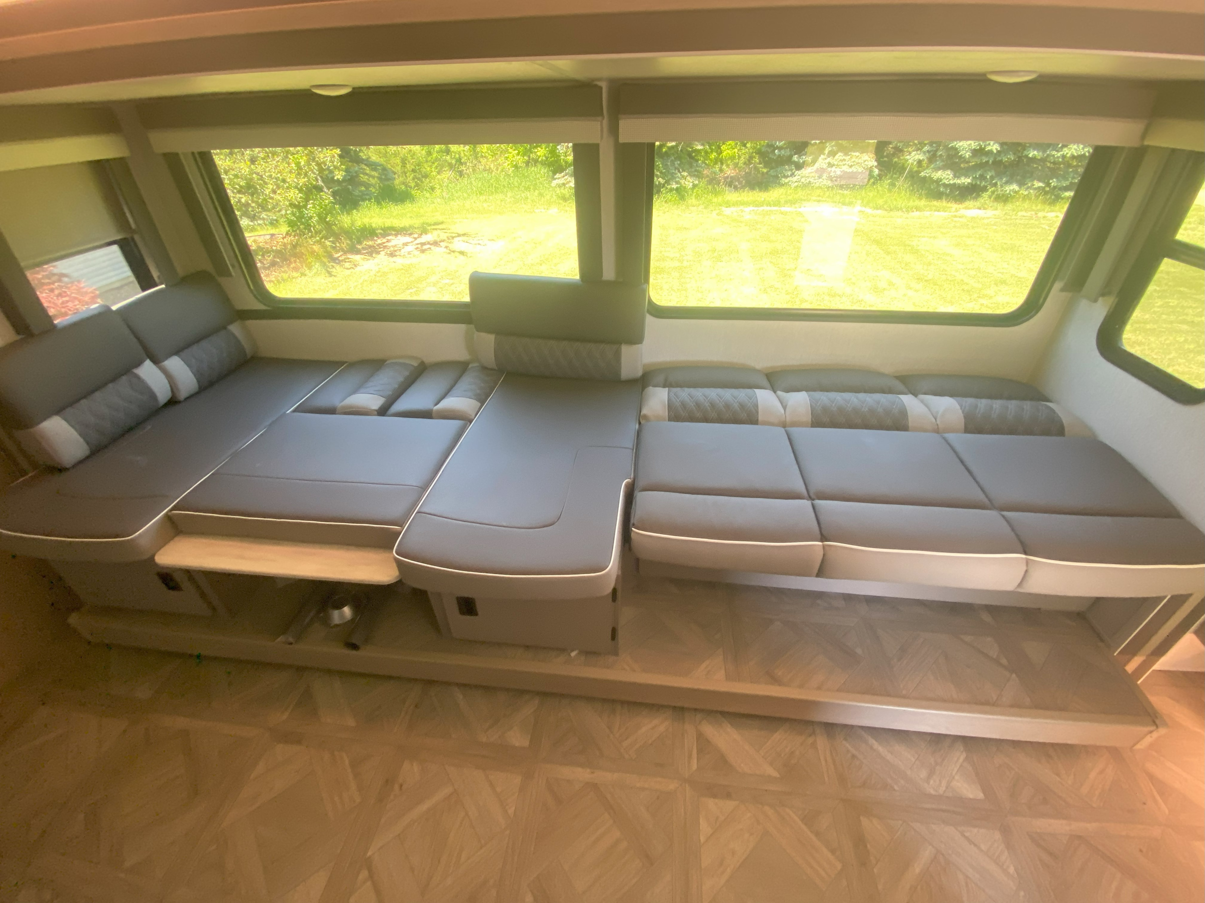 Spacious rv rental interior: neutral convertible seating, light wood floor, and large windows with green outdoor view.. Forest River Wildwood X-Lite Platinum 2023