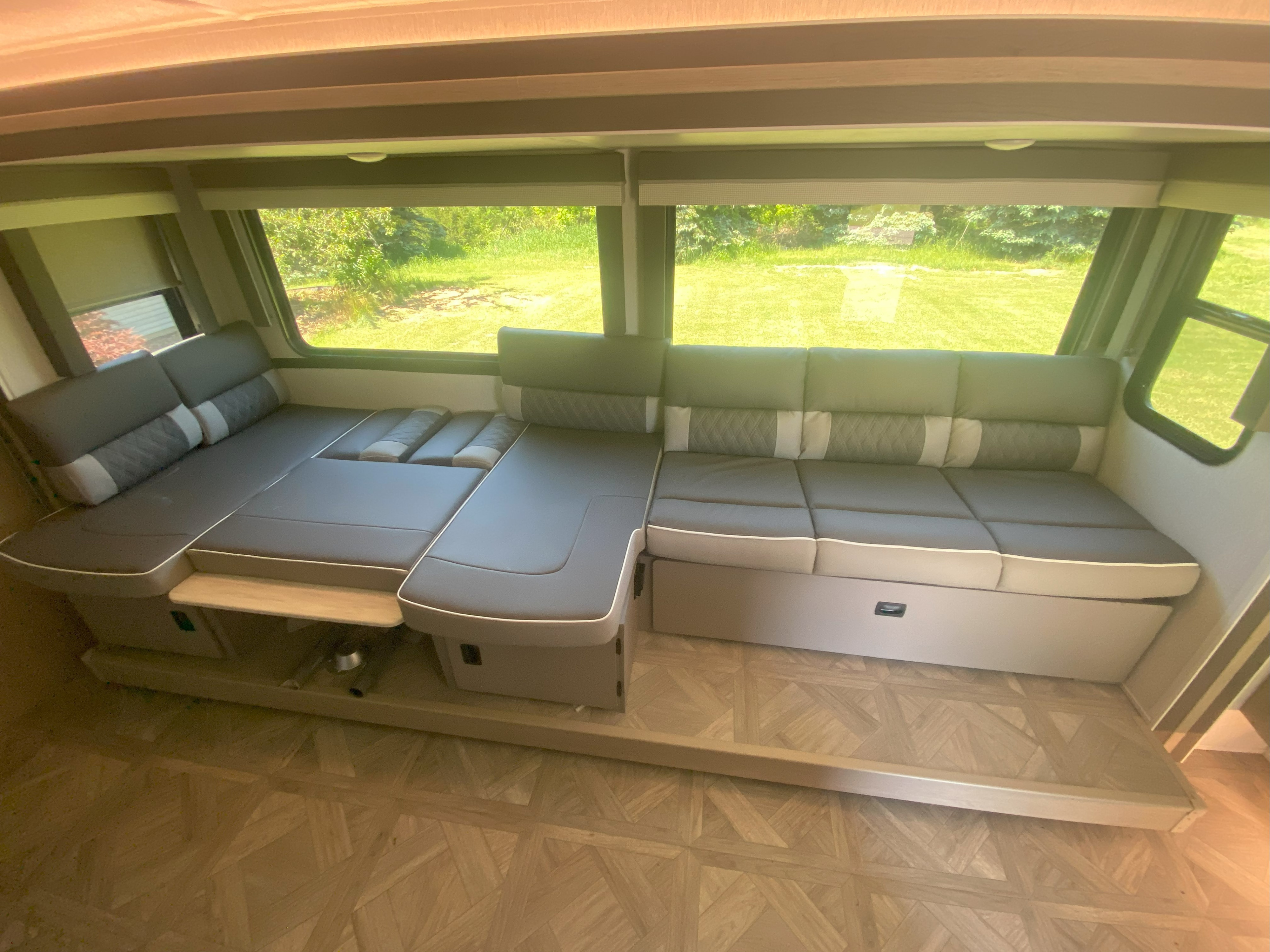 Spacious RV rental interior with a versatile gray dinette and large windows showing a lush outdoor view, perfect for travel comfort.. Forest River Wildwood X-Lite Platinum 2023