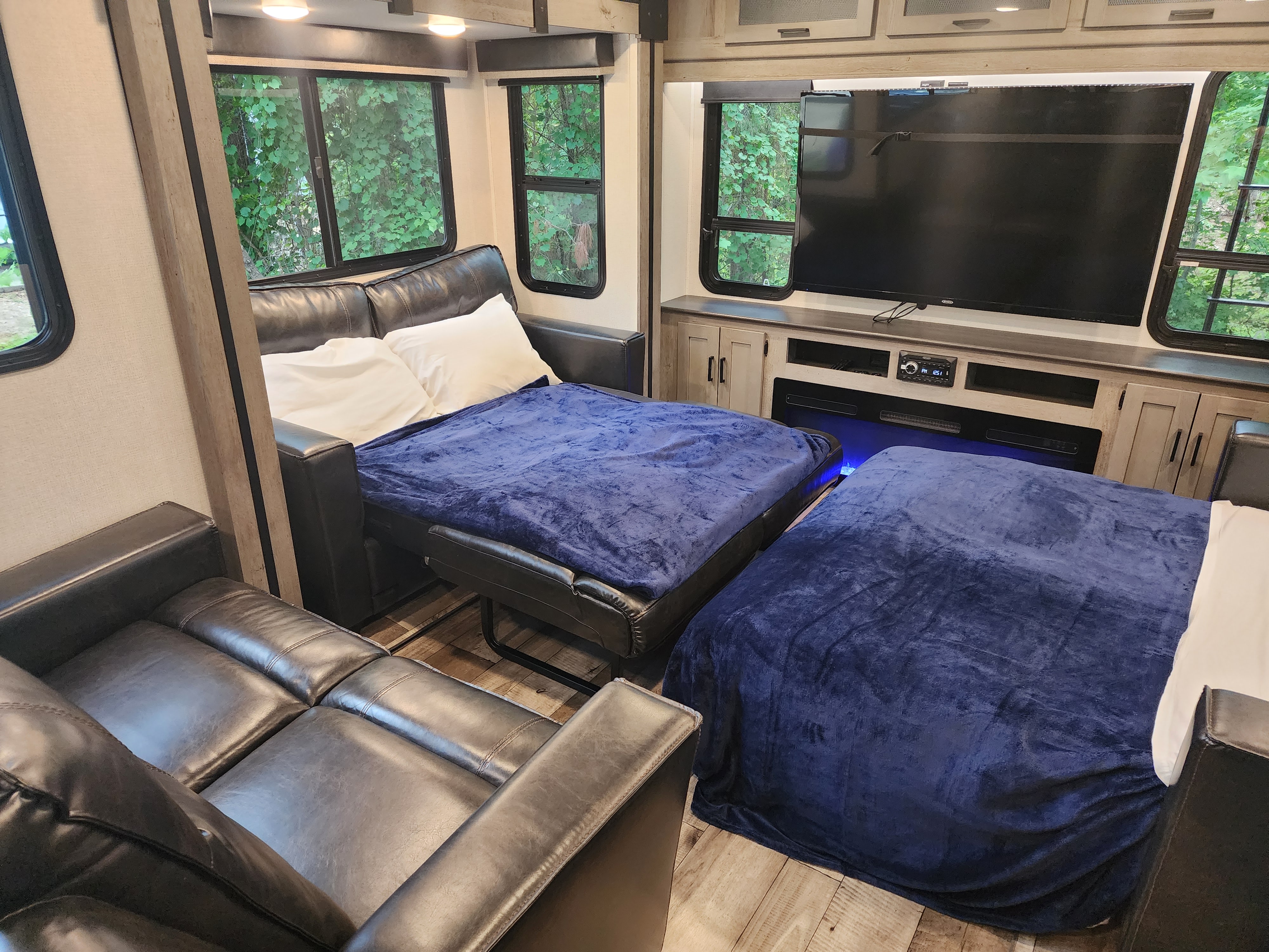 Inside a modern RV rental, two beds are made up with blue blankets. A TV & entertainment center complete the cozy living space.. Keystone RV Outback 2021