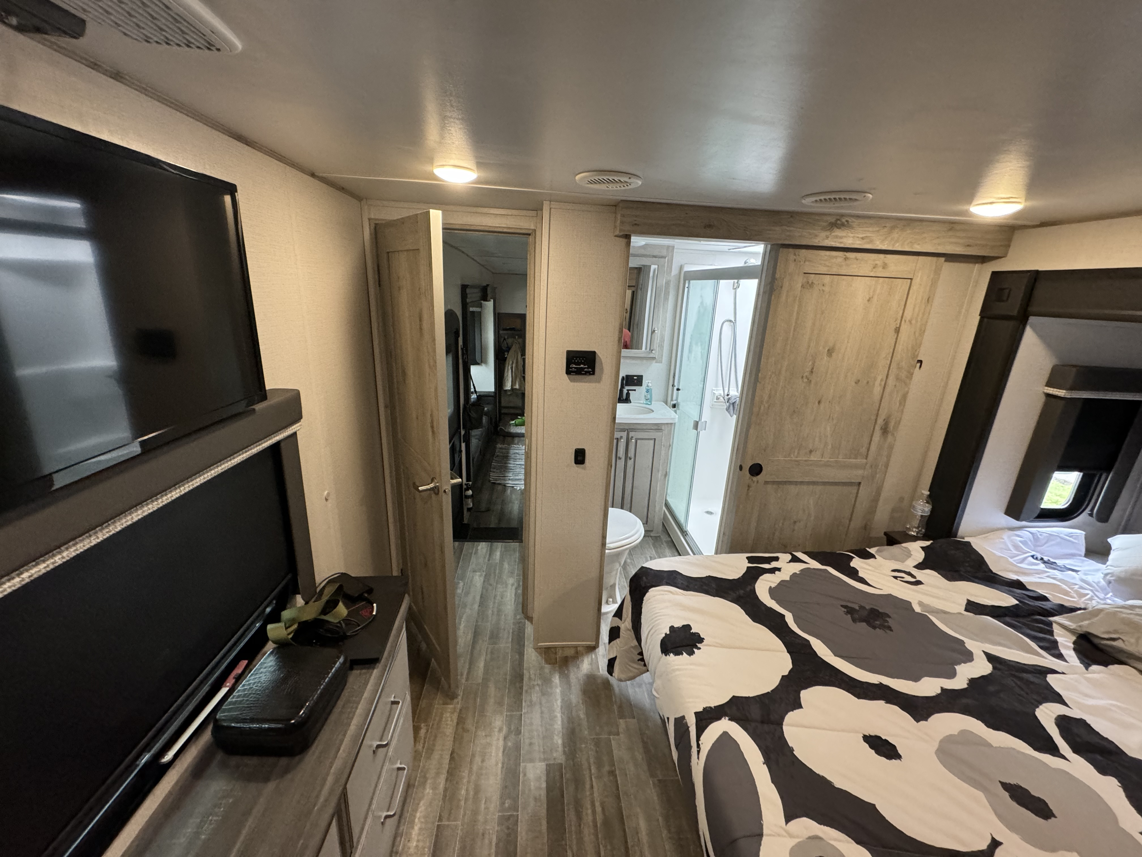 Explore this modern RV rental interior, featuring a bedroom with a bold patterned bed, TV, and a connected bathroom with shower.. Keystone RV Avalanche 2021