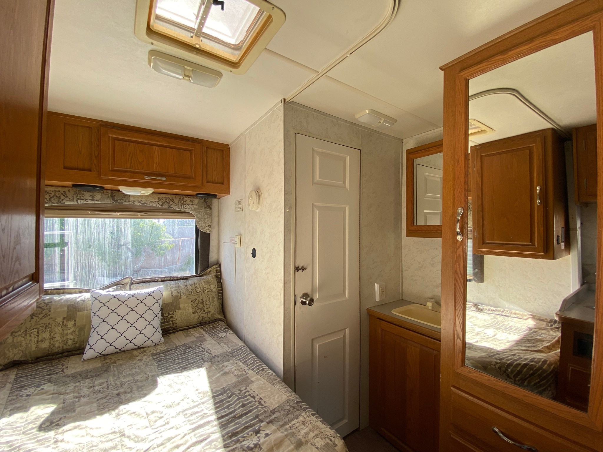 Inside this RV rental: a bright bedroom with a comfy bed, window view, and wooden cabinetry, creating a cozy travel space.. Four Winds 5000 2003