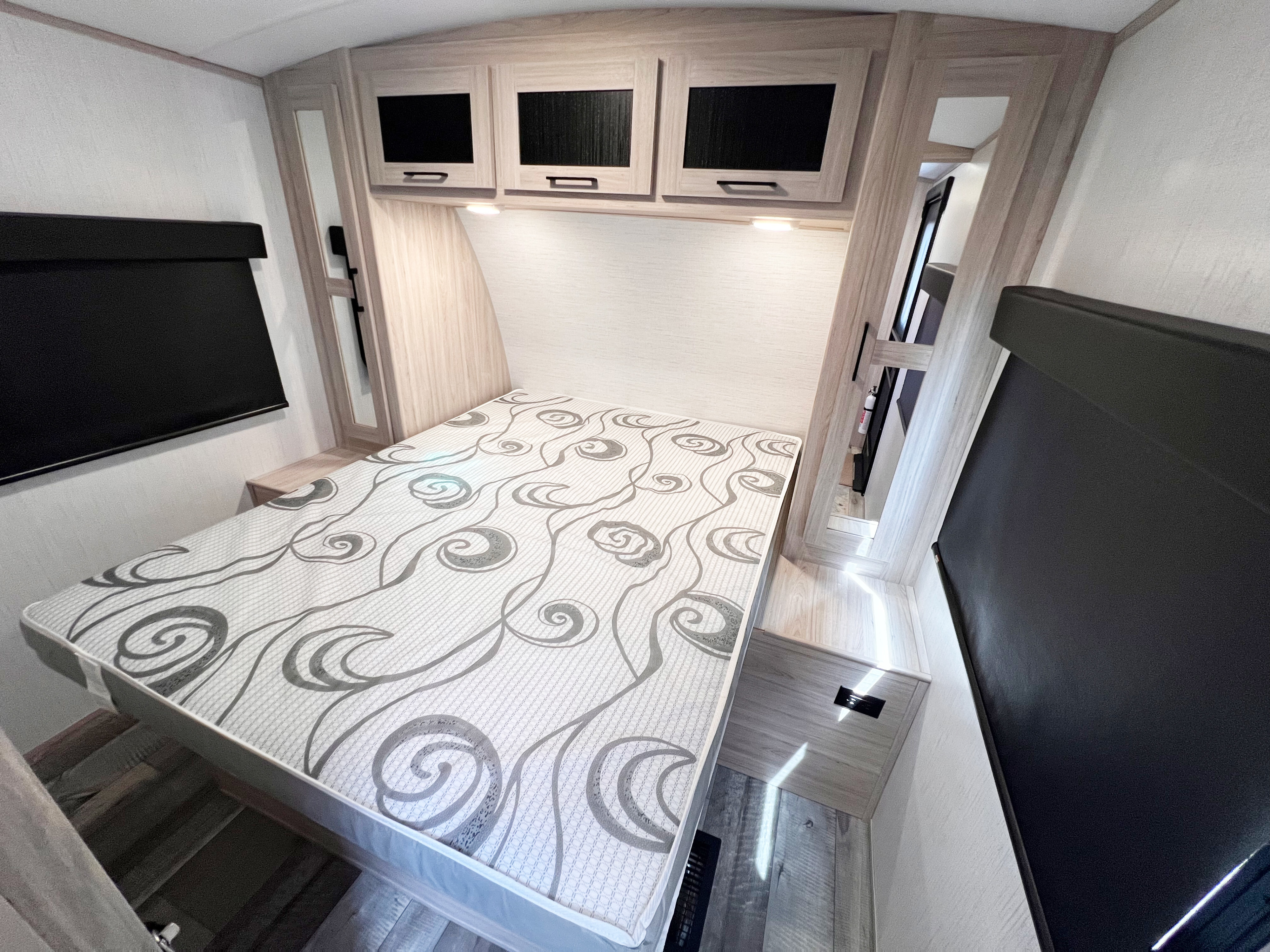 Bright RV rental bedroom with patterned bed, light wood cabinets, and dark window shades.. Heartland Sundance 2022