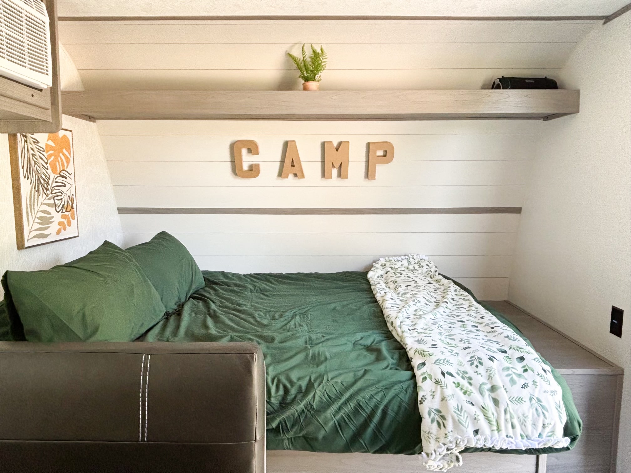 Cozy RV rental bedroom with green bedding, 'CAMP' sign, and a leafy blanket, providing comfort for your journey.. Dutchmen Coleman 17B 2024