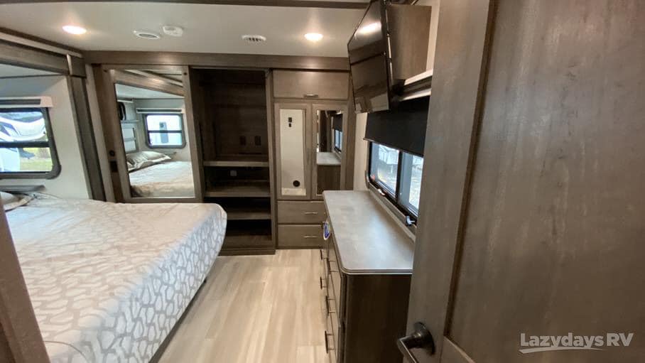 Modern RV bedroom interior, perfect for comfortable RV rental stays. Includes bed, dresser, TV, and mirrored closet.. Grand Design Solitude 2022