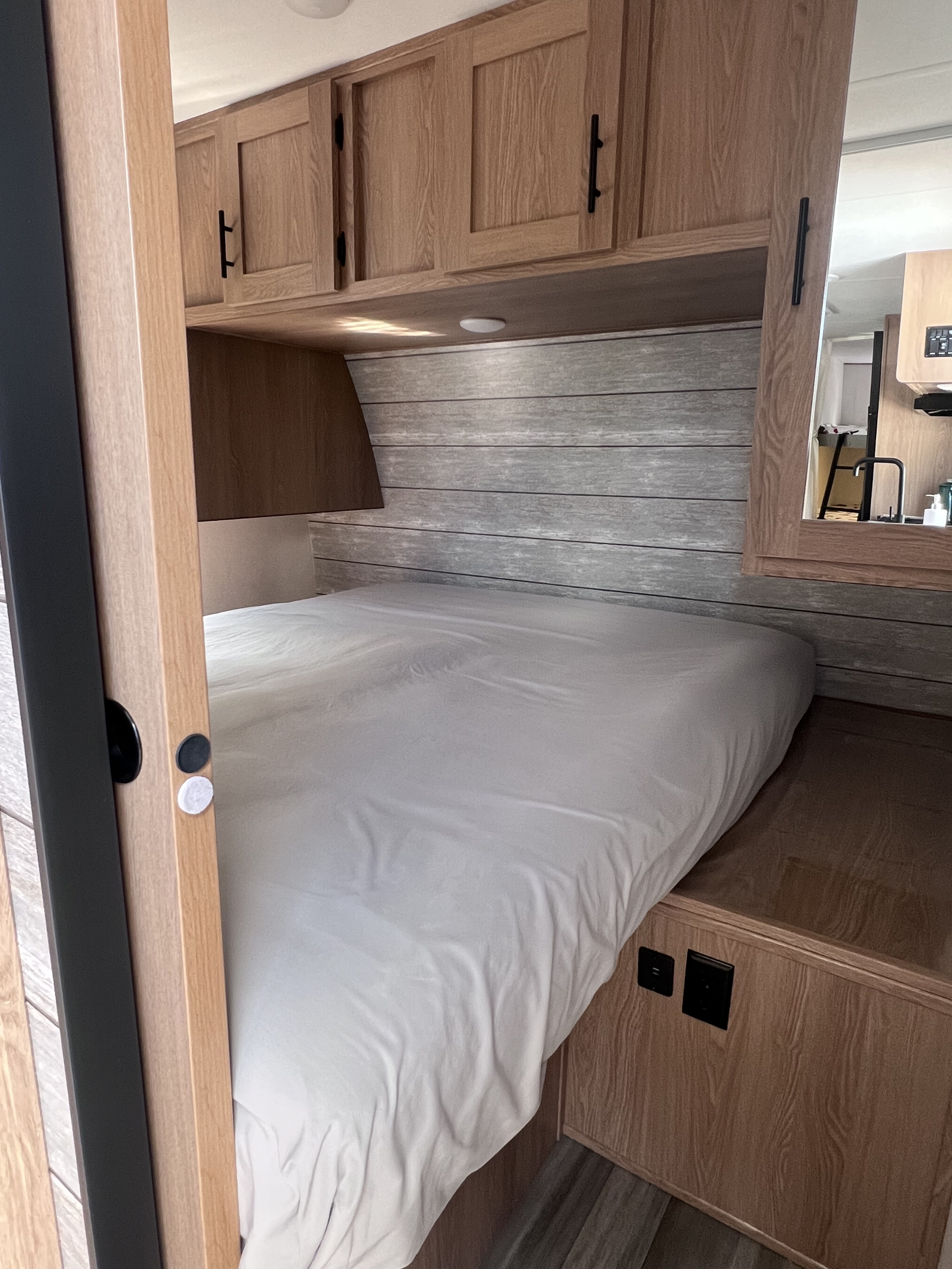 This RV rental bedroom offers a clean bed, natural wood cabinets, and a modern planked headboard with power outlets.. Prime Time Avenger 24 BHS 2023