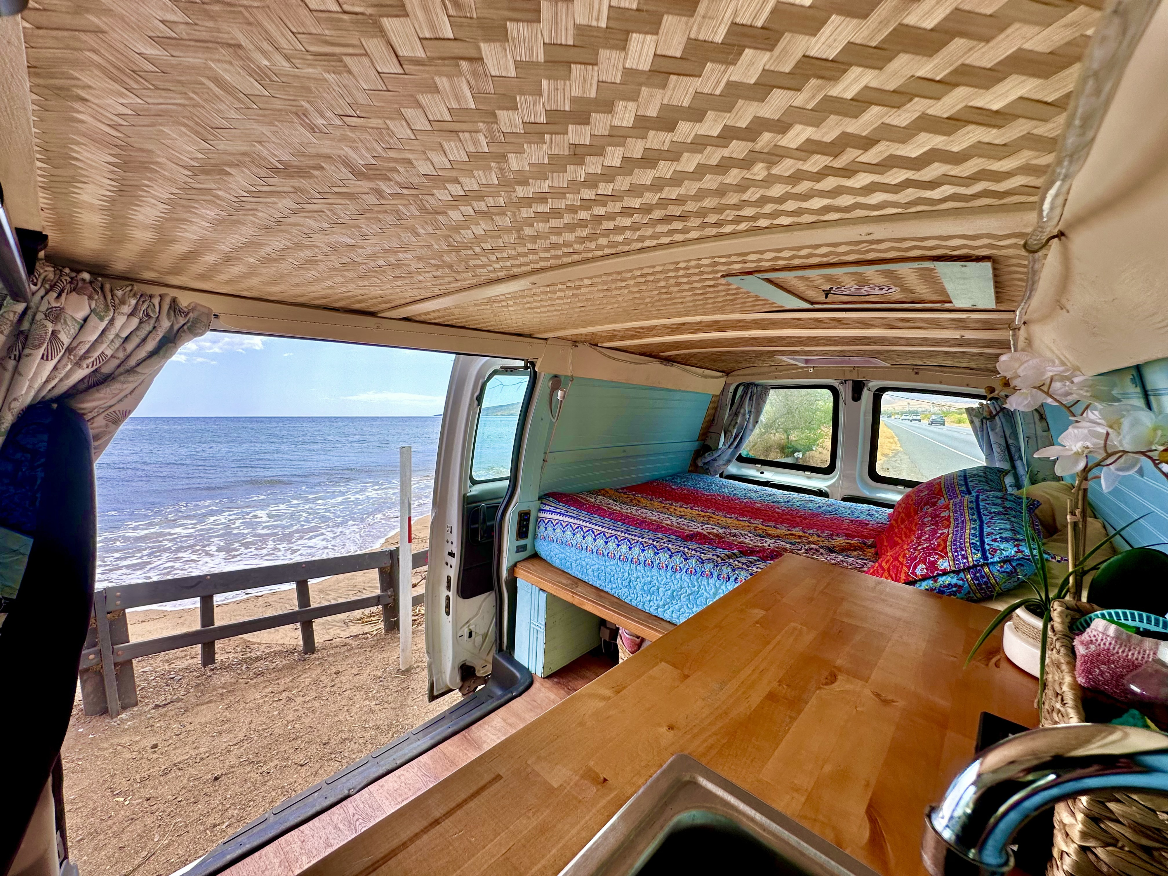 Cozy RV rental interior by the ocean features a woven ceiling, colorful bedding, and a wooden counter with a sink.. Gmc Savanna 2006