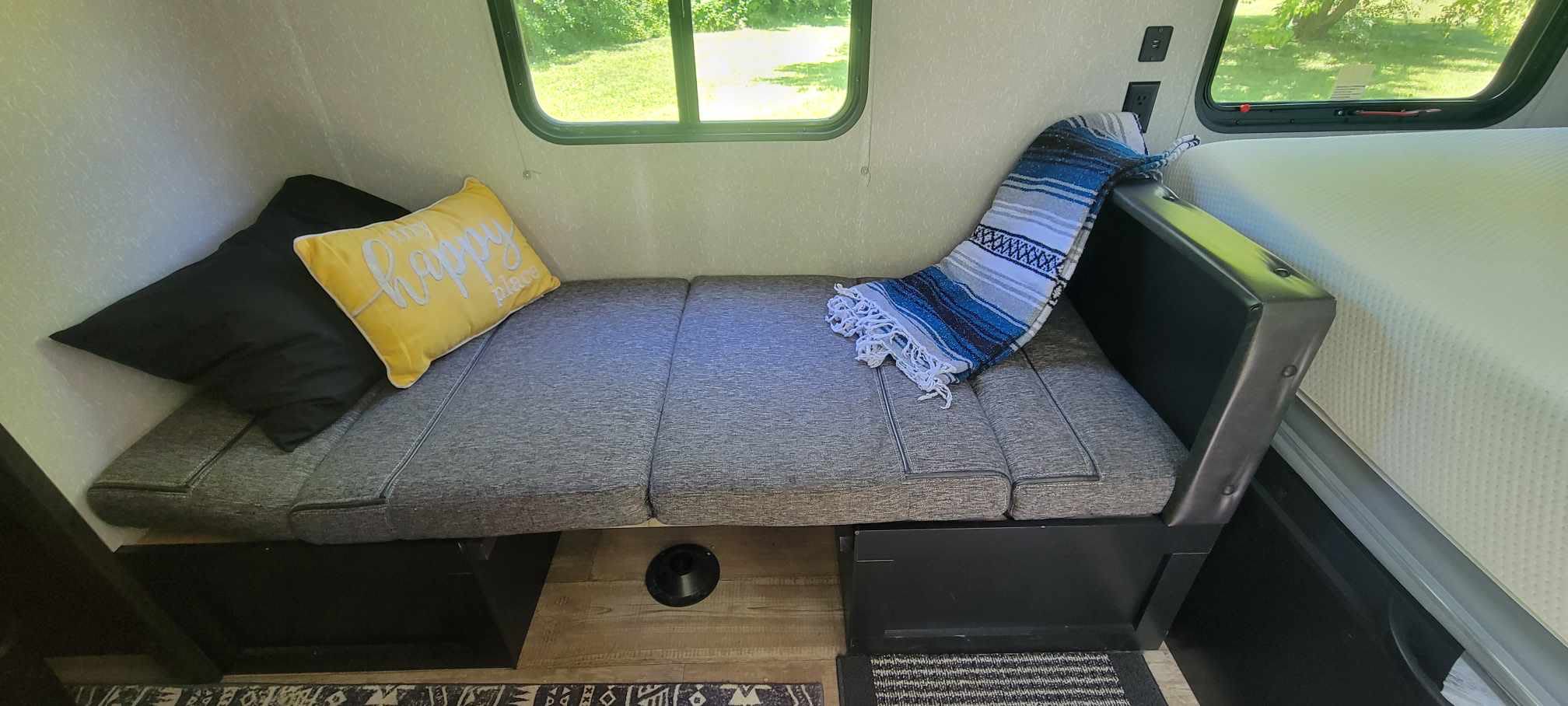 Inside an RV rental: a comfy gray bench/bed with black and yellow pillows, a striped blanket, and a window view.. Forest River Cherokee Wolf Pup 2022