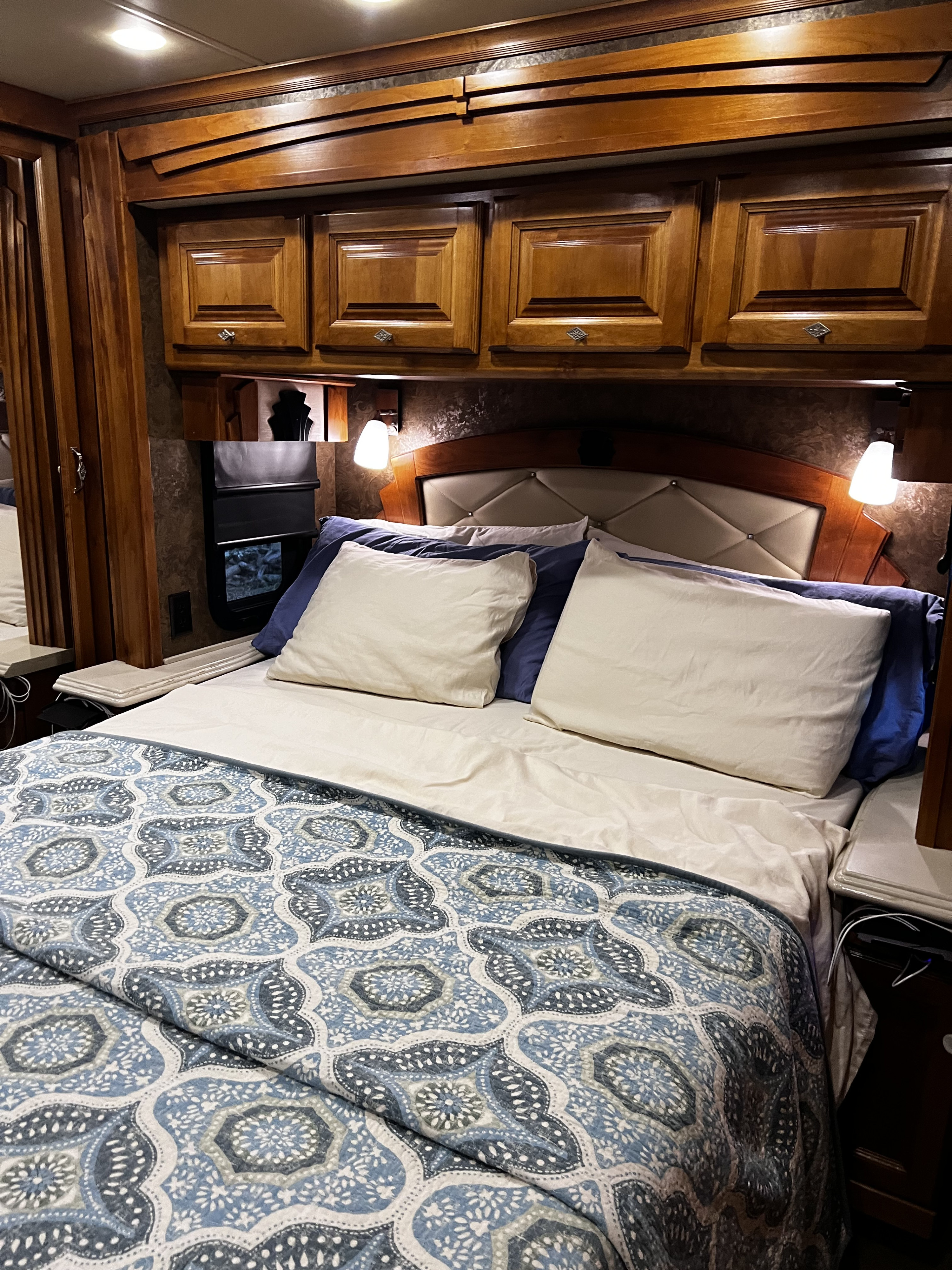 Cozy RV rental bedroom with a patterned blue and white bedspread, comfy pillows, and rich wooden cabinetry overhead.. Allegro Allegro Motorhome 2015