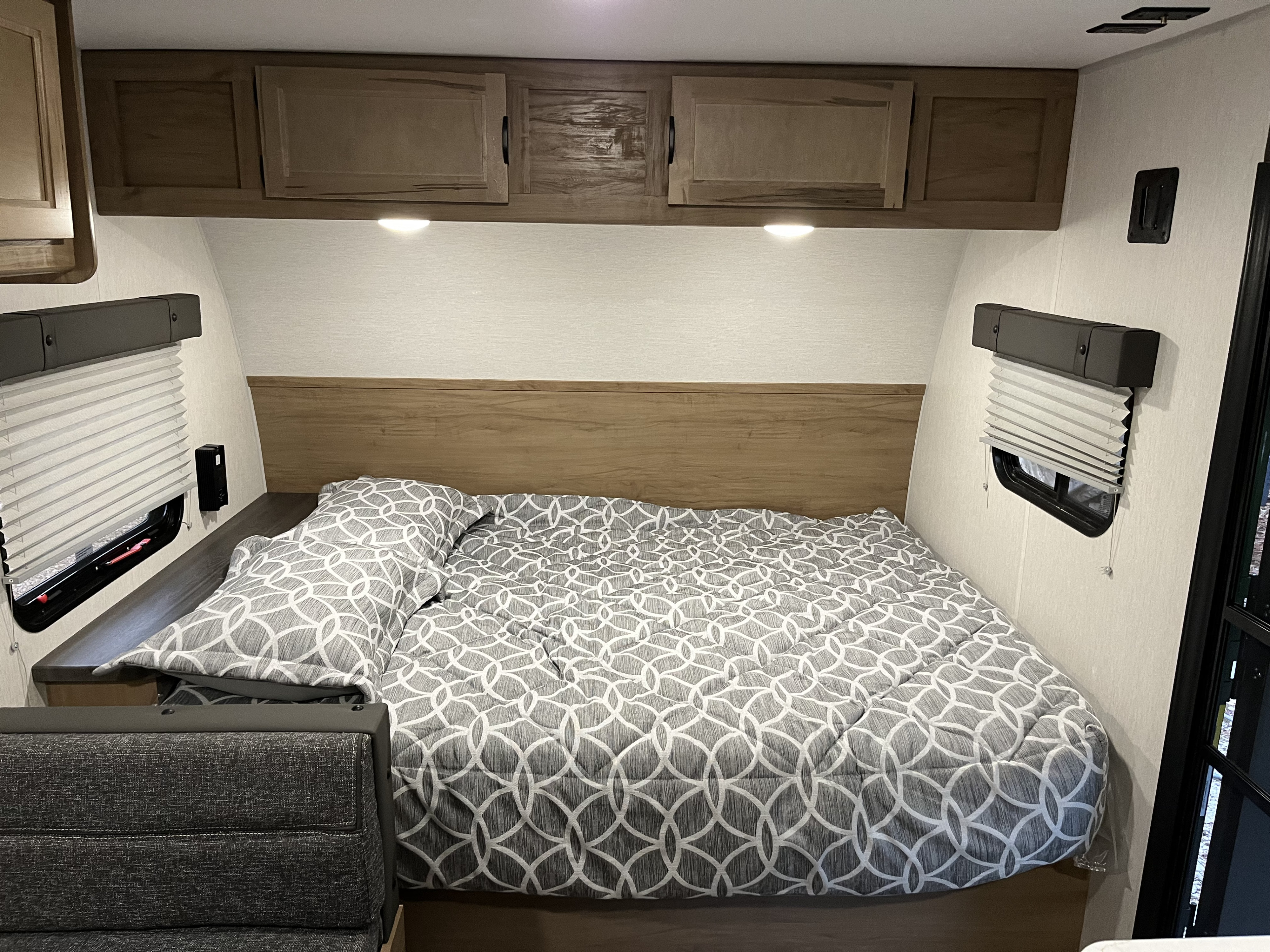 Cozy RV rental bedroom: patterned bed, overhead cabinets with lights, and side window blinds.. Forest River Cherokee Wolf Pup 16BHS 2024