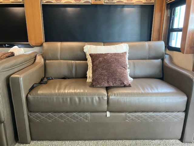 Comfortable taupe leather RV sofa with decorative pillows & seatbelt, ideal for your RV rental adventures.. Fleetwood Southwind 37H 2018