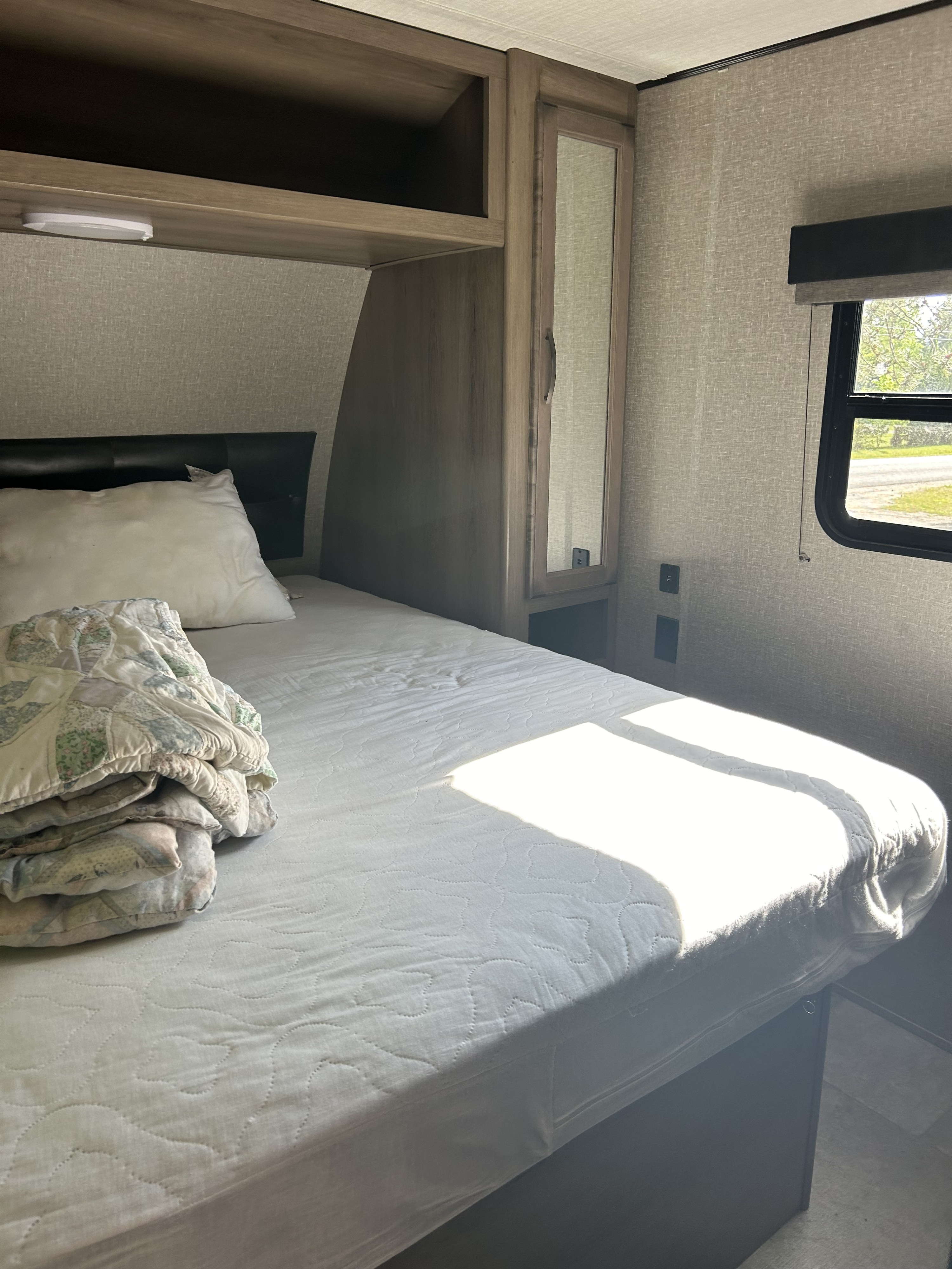 RV rental bedroom with a sunlit bed, quilted mattress cover, folded quilt, mirrored wardrobe, and overhead storage.. Travel Lite Other 2020
