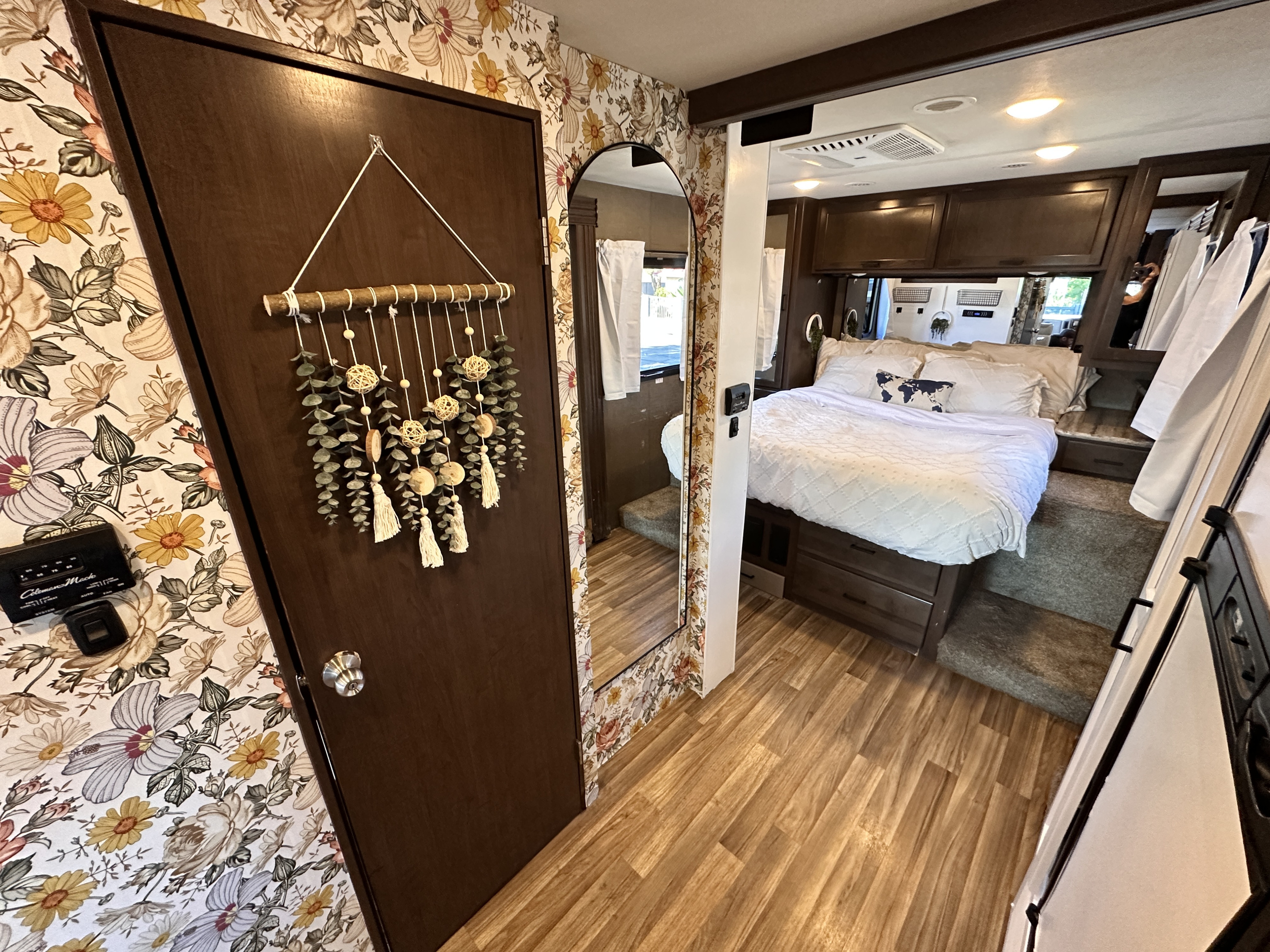 Charming RV rental interior featuring a cozy bedroom with floral wallpaper, wood flooring, and a macrame wall hanging.. Thor Motor Coach A.C.E 2018