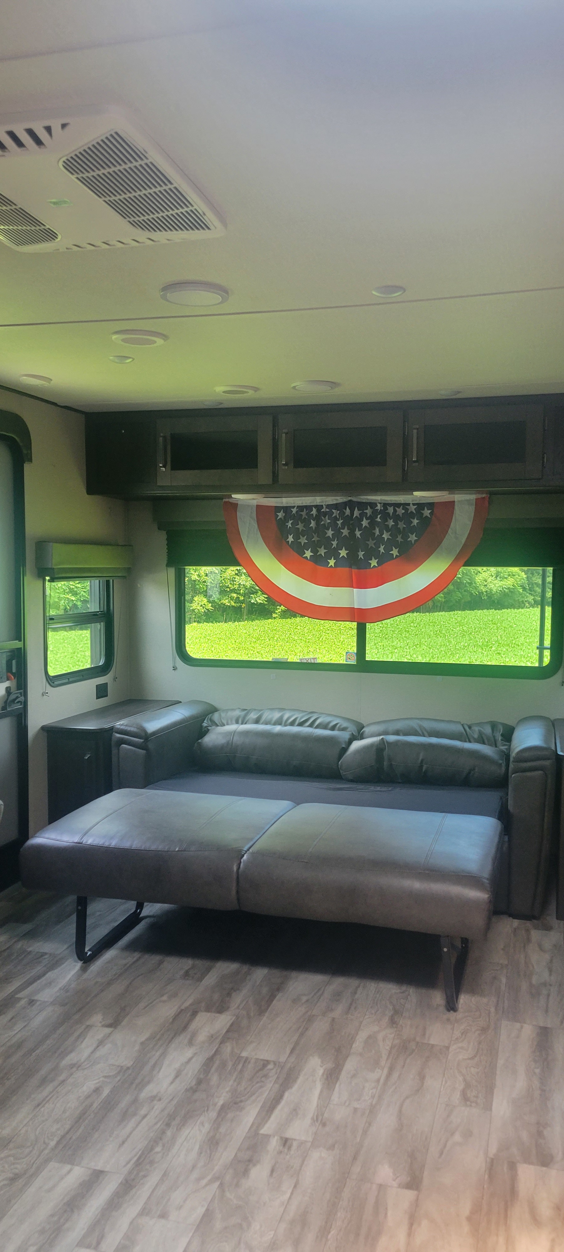 RV rental interior: comfy sofa bed extended, wood floors, and bright windows with a view. Perfect camper living space.. Grand Design Transcend 2021