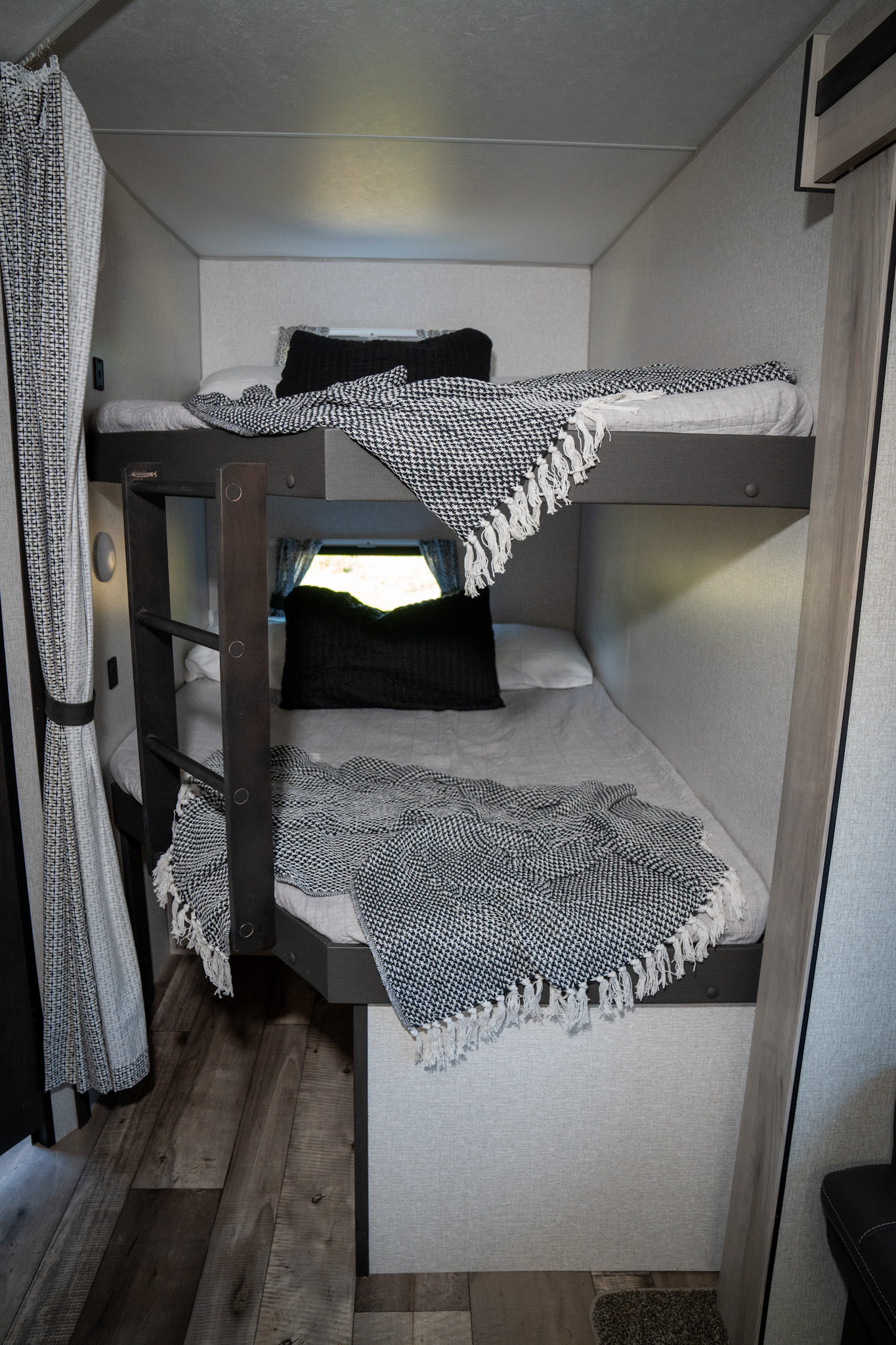 RV rental bunk beds: cozy grey bedding, black pillows, a black/white throw, and a sturdy access ladder visible.. KZ Connect 2021