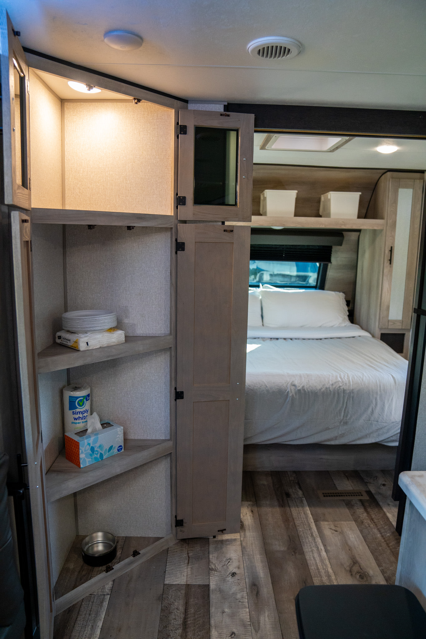 Inside an RV rental: a bedroom with organized storage shelves holding supplies like paper plates, tissues, and a pet bowl.. KZ Connect 2021
