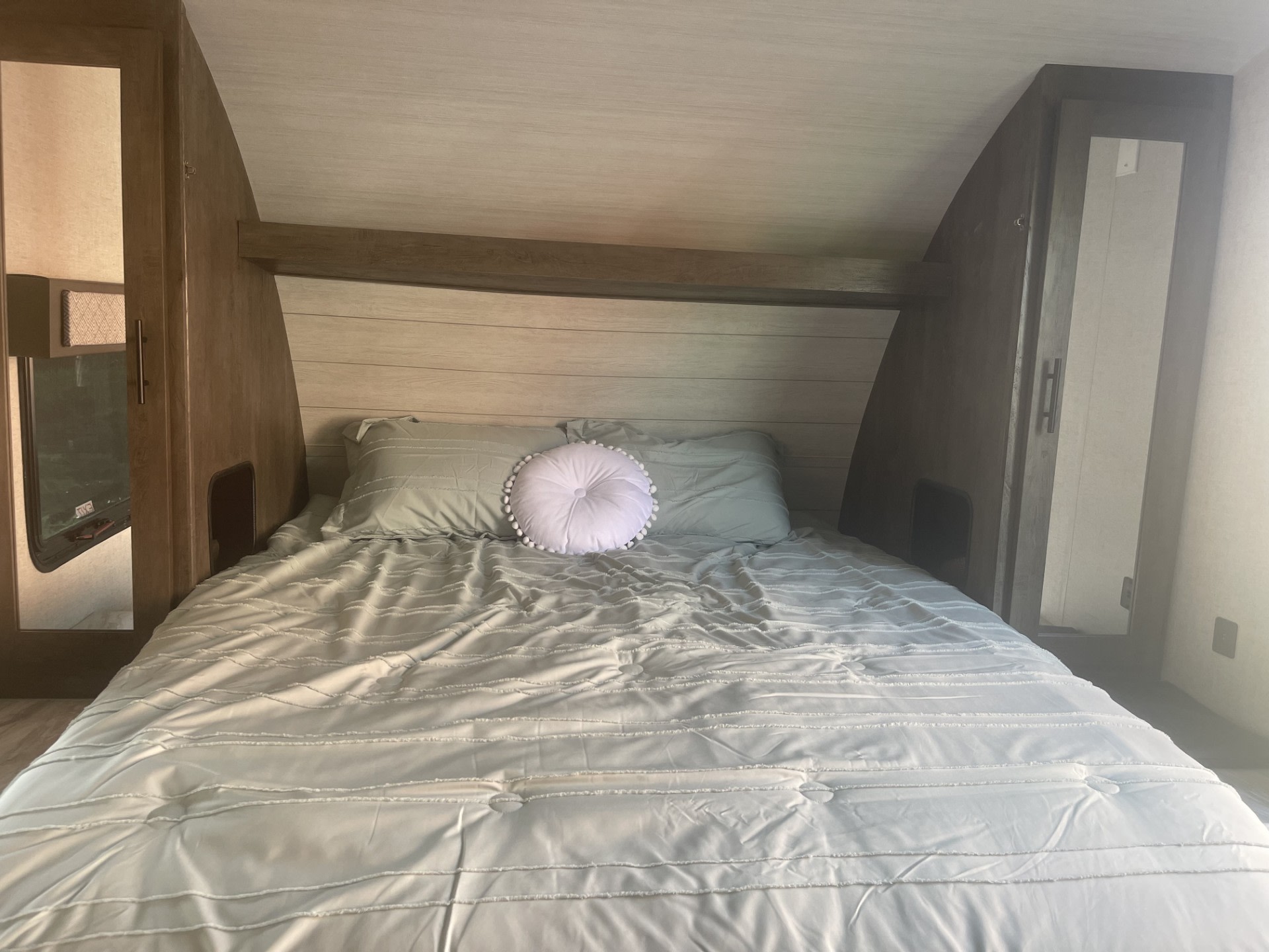 Comfortable bed with light green bedding in an RV rental. Wood cabinets and ceiling add to the cozy RV interior, perfect for travel.. Forest River Wildwood X-Lite 2021