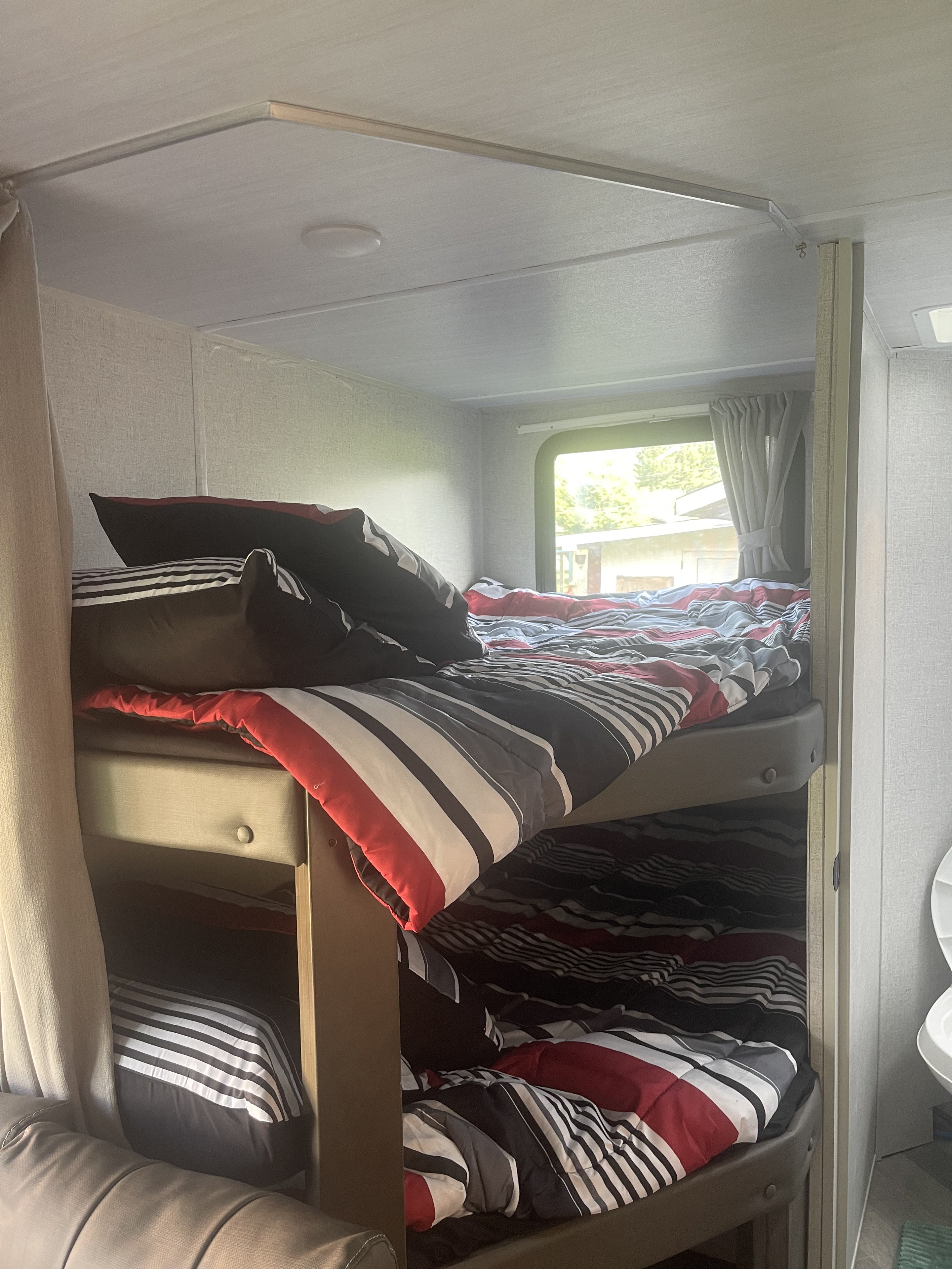 RV rental interior features cozy bunk beds with striped bedding, providing a comfortable sleeping area for travelers.. Forest River Wildwood X-Lite 2021
