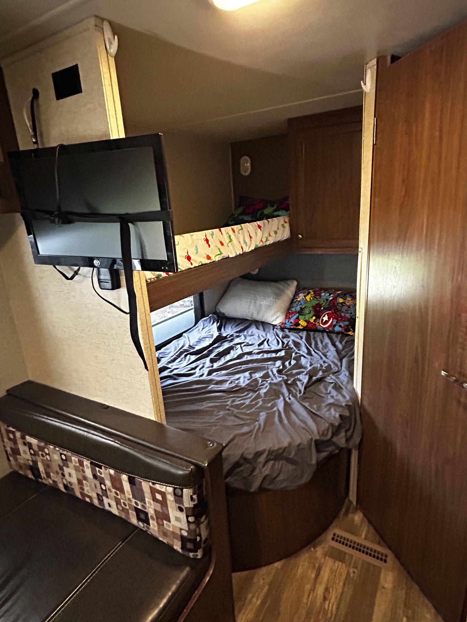 Compact RV rental interior: upper & lower bunk beds, mounted TV, and patterned bench seating. A functional family space.. Heartland RVs Pioneer 2016